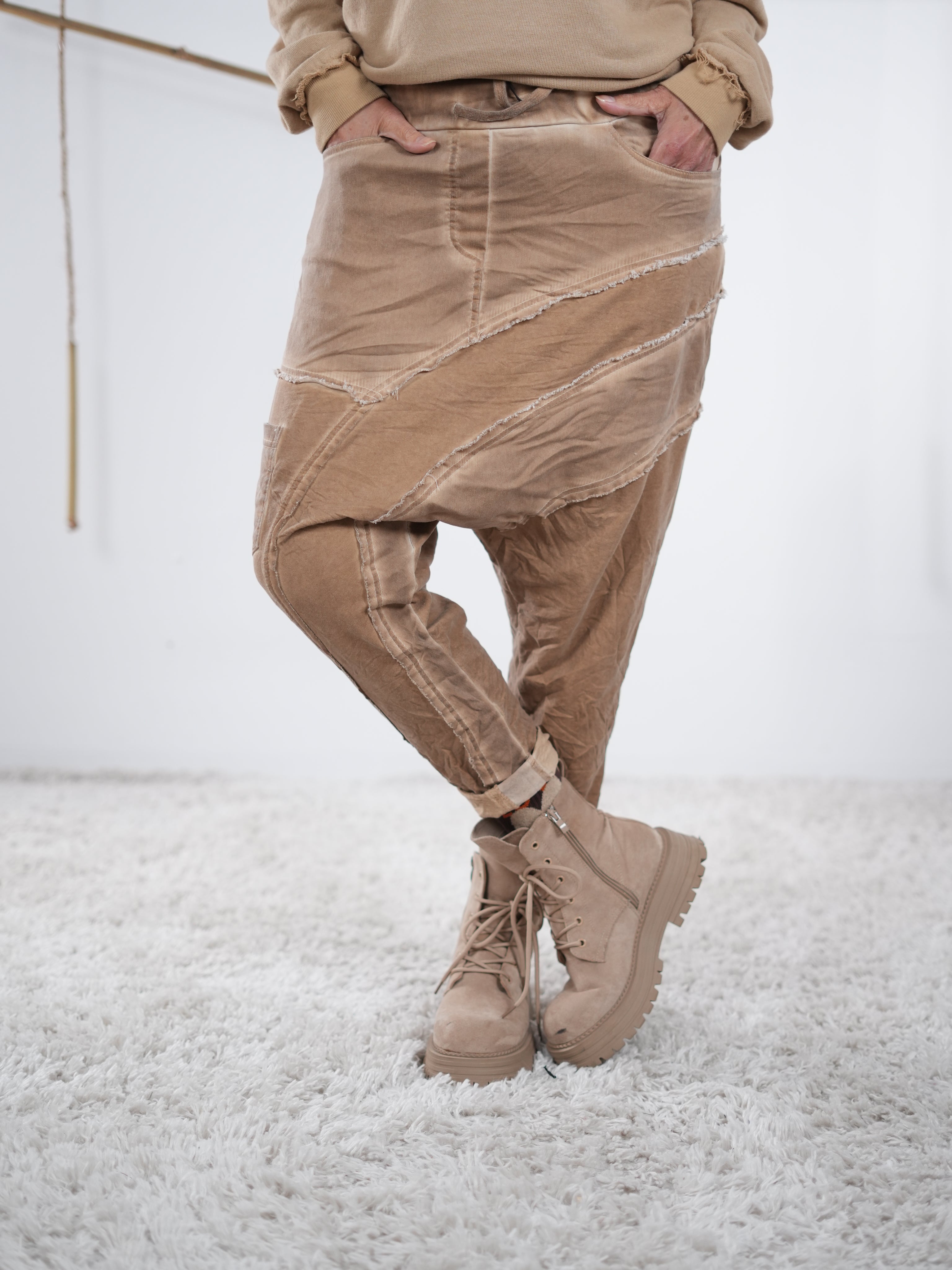 Camelfarbene Baggyhose mit asymmetrischen Nähten und lässigem Fall, getragen mit beigefarbenen Boots.