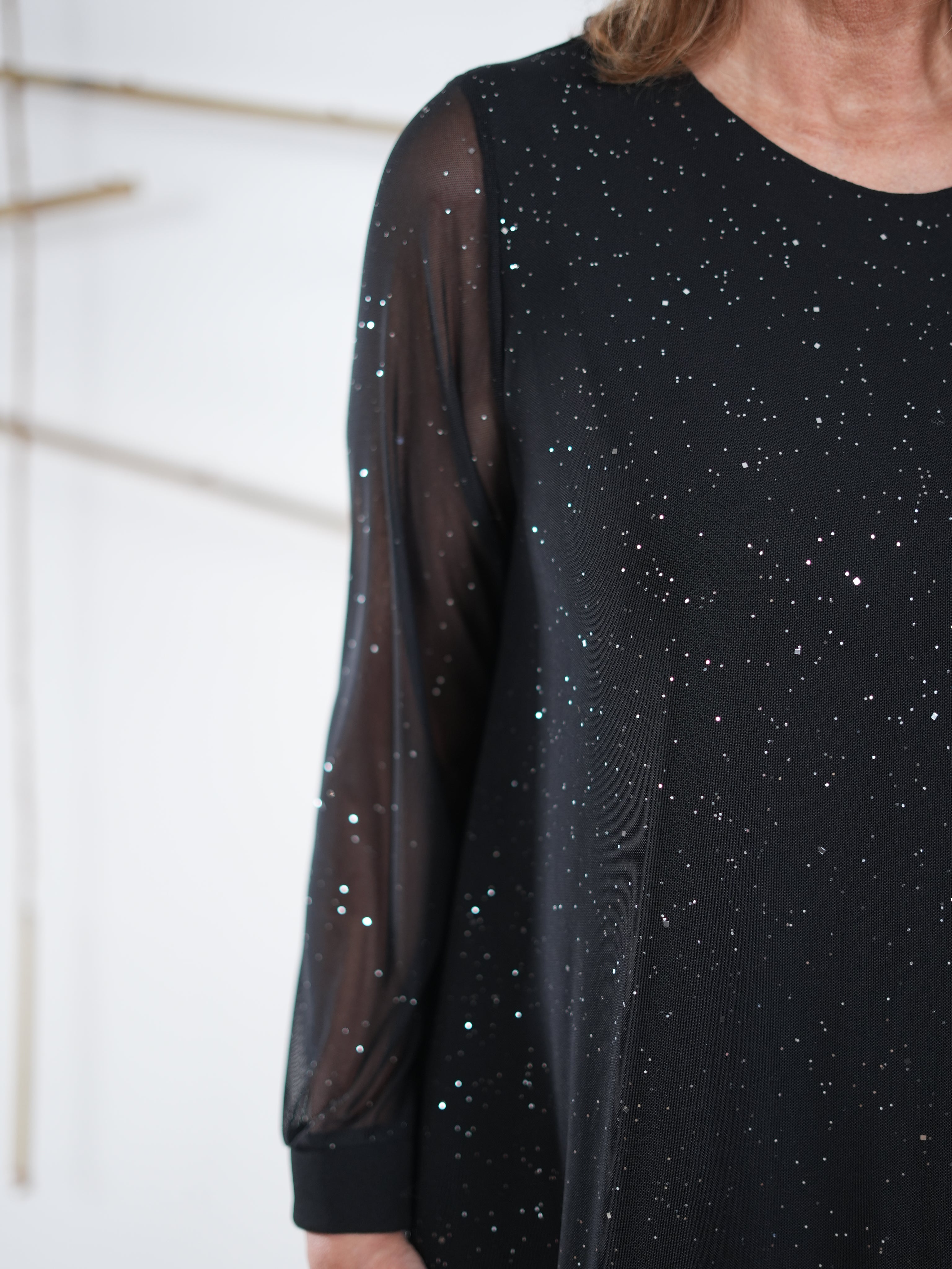 Seitenansicht eines schwarzen Glitzerkleids mit Mesh-Ärmeln und Kunstleder-Saum