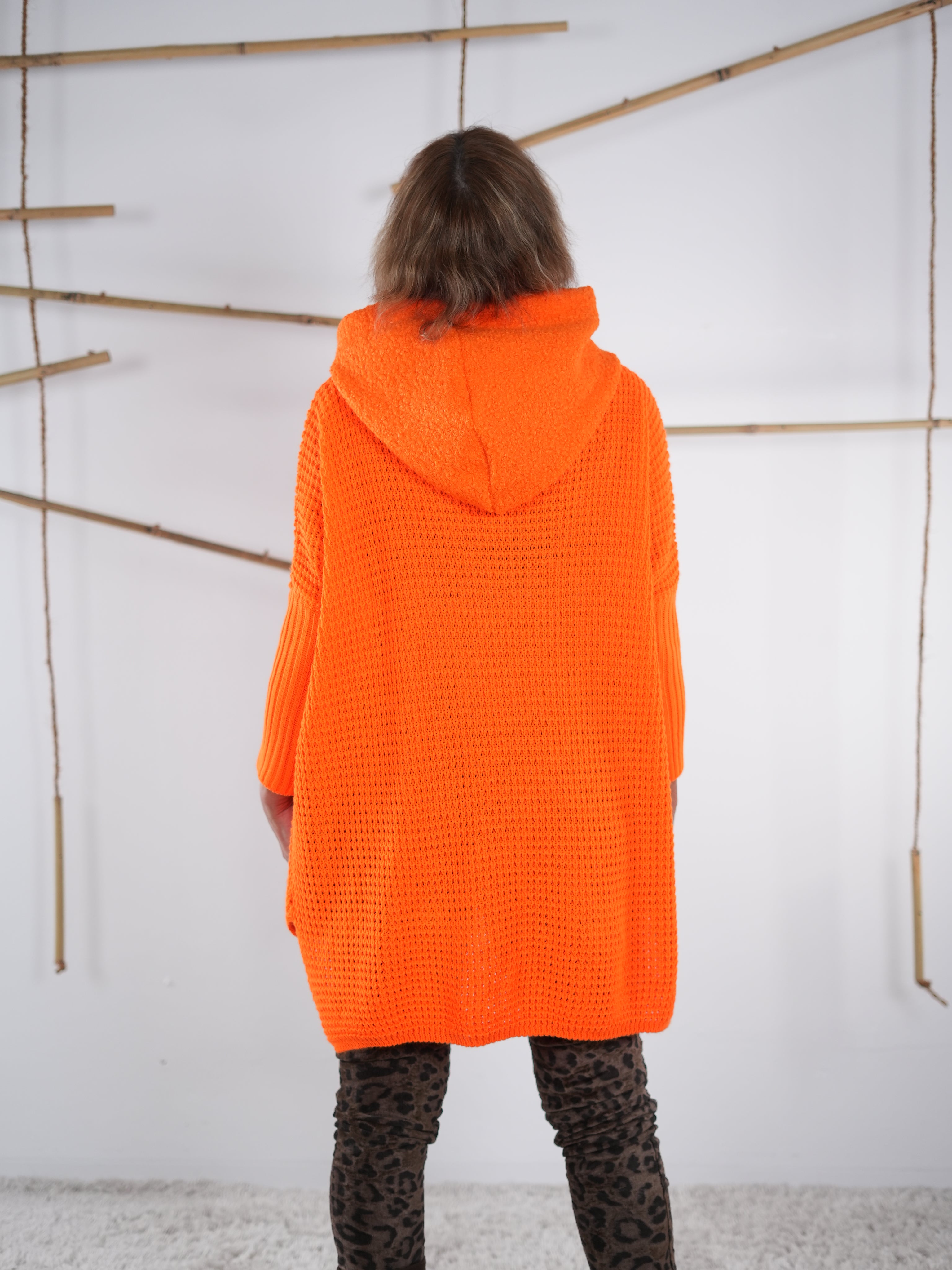 Rückansicht eines orangefarbenen Grobstrickpullis mit Kapuze und Vokuhila-Schnitt.