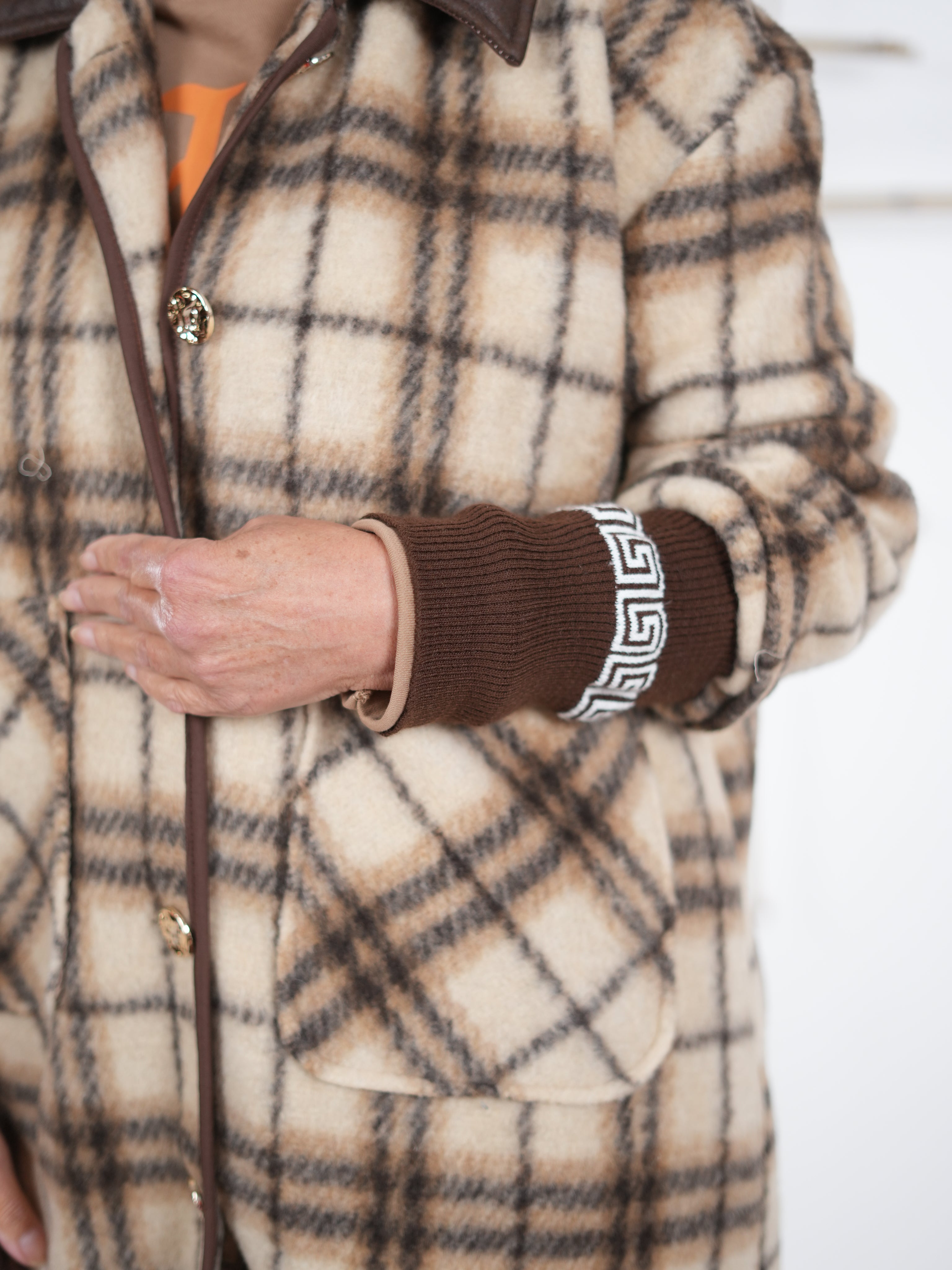 Nahaufnahme eines beigebraunen karierten Fleece-Mantels mit braunen Strickbündchen und dekorativem Muster am Ärmel, getragen von einer Frau im Studio.