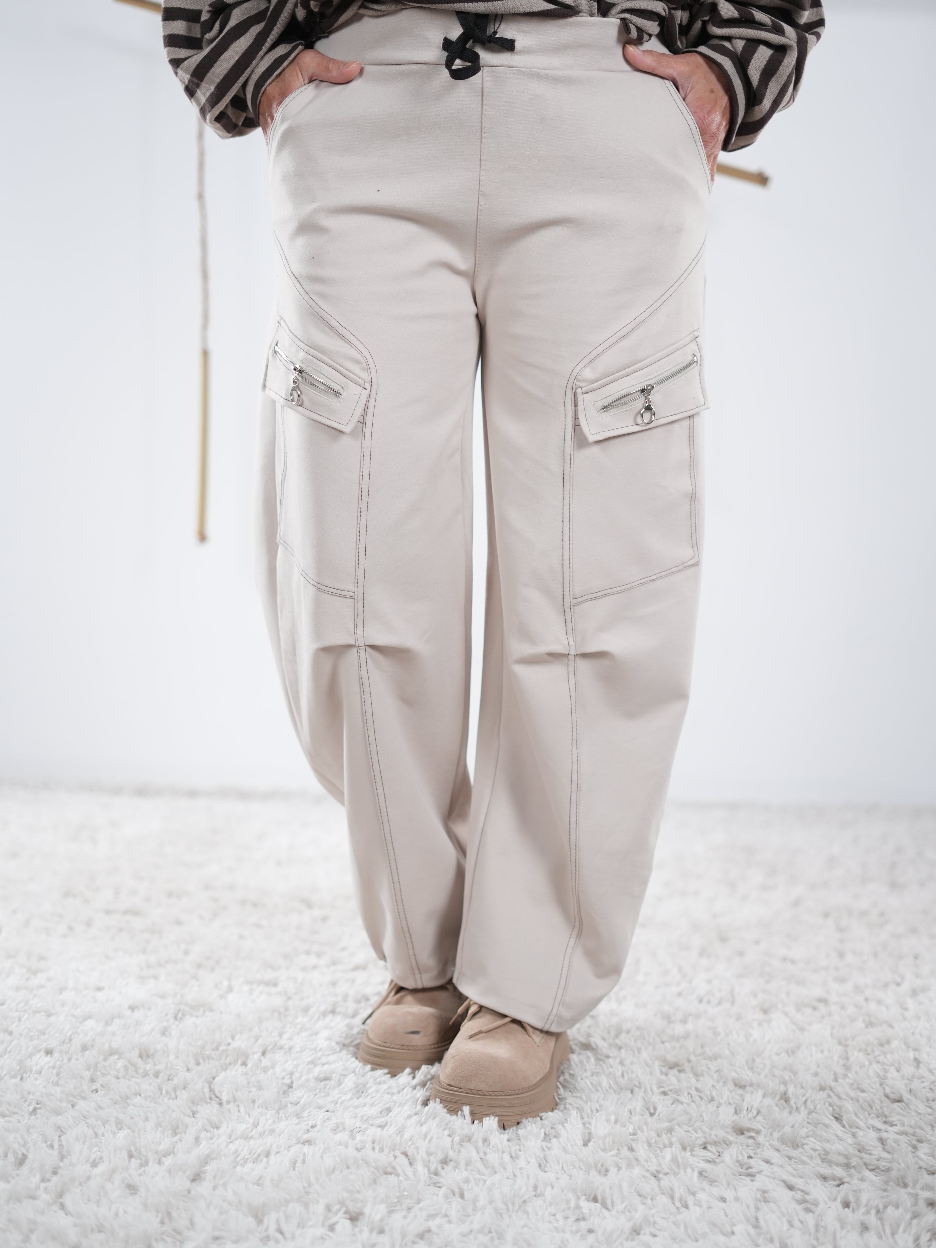 Beigefarbene Wide-Leg-Hose mit Kontrastnähten und seitlichen Reißverschlusstaschen, frontale Ansicht