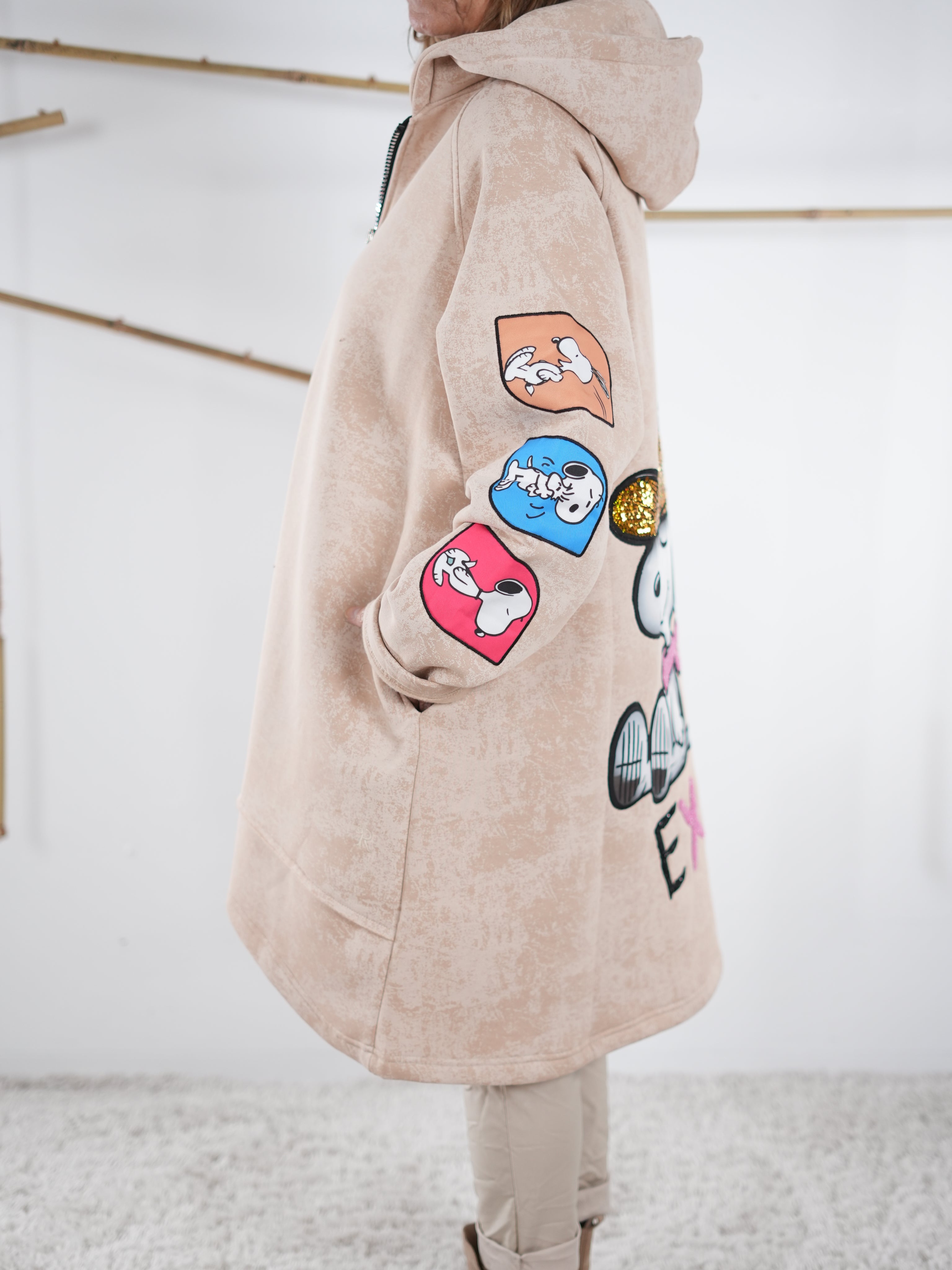 Comic-Patches am Ärmel eines beige Oversize-Mantels, Nahaufnahme