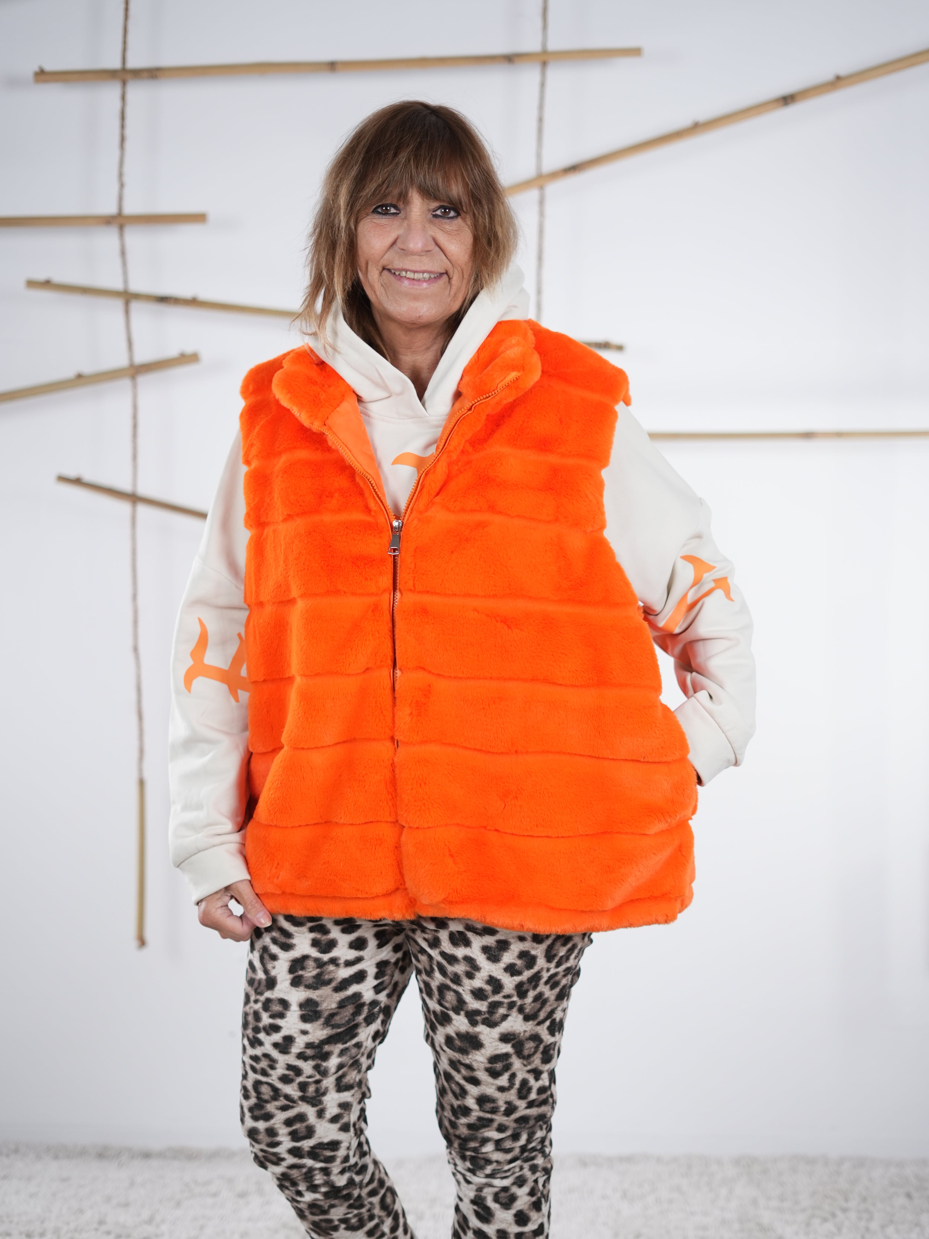 Orangefarbene Flausch-Weste mit Zipper in der Frontansicht, weich strukturiert mit seitlichen Eingriffstaschen, im geschlossenem Zustand