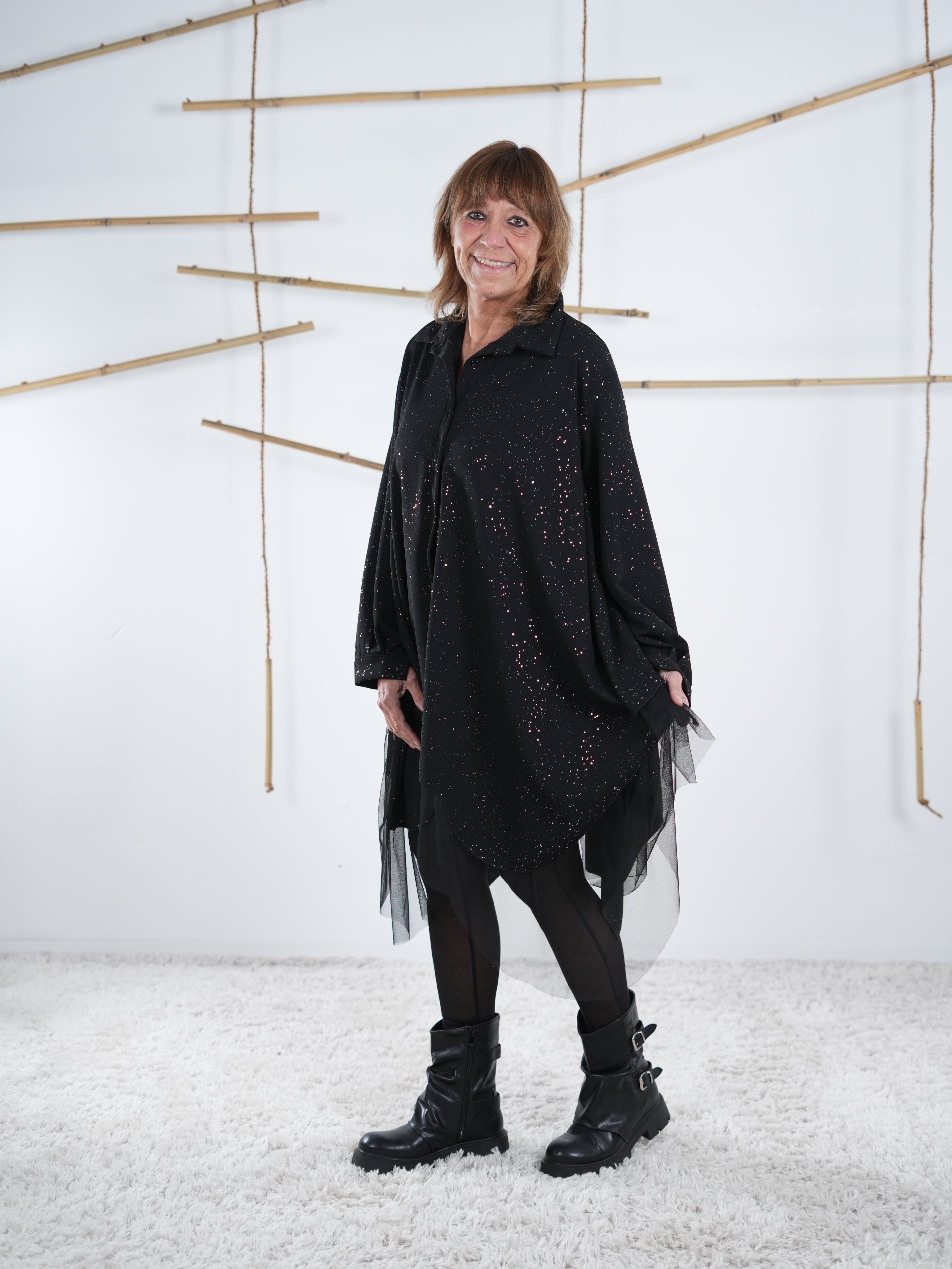 Seitliche Aufnahme der schwarzen Tunika mit Glitzer Elementen. Der weite Schnitt der Tunika fällt zudem auf .