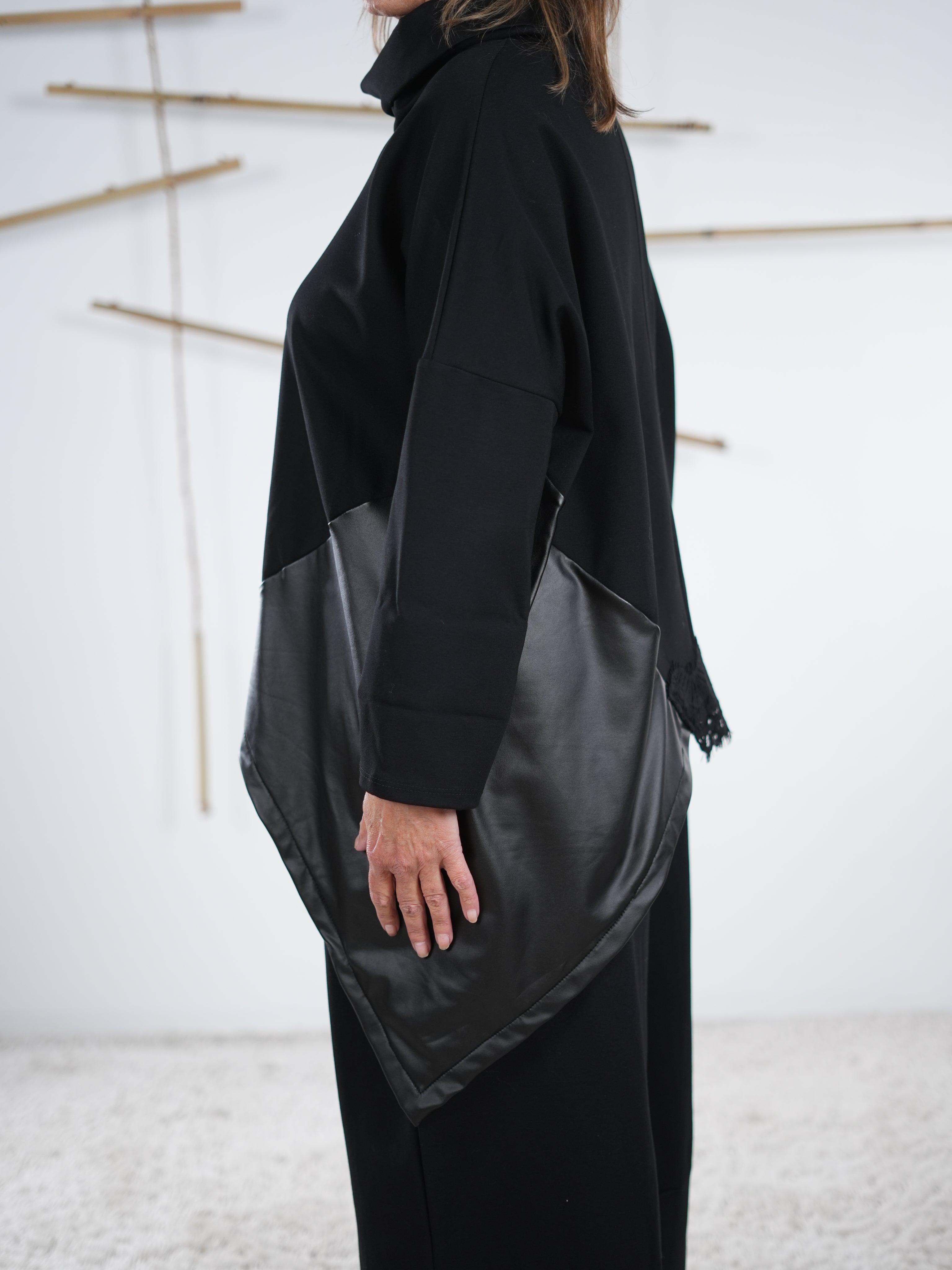 Seitliche Ansicht eines schwarzen, weiten Pullis mit Kunstlederelement und überschnittenem Arm.