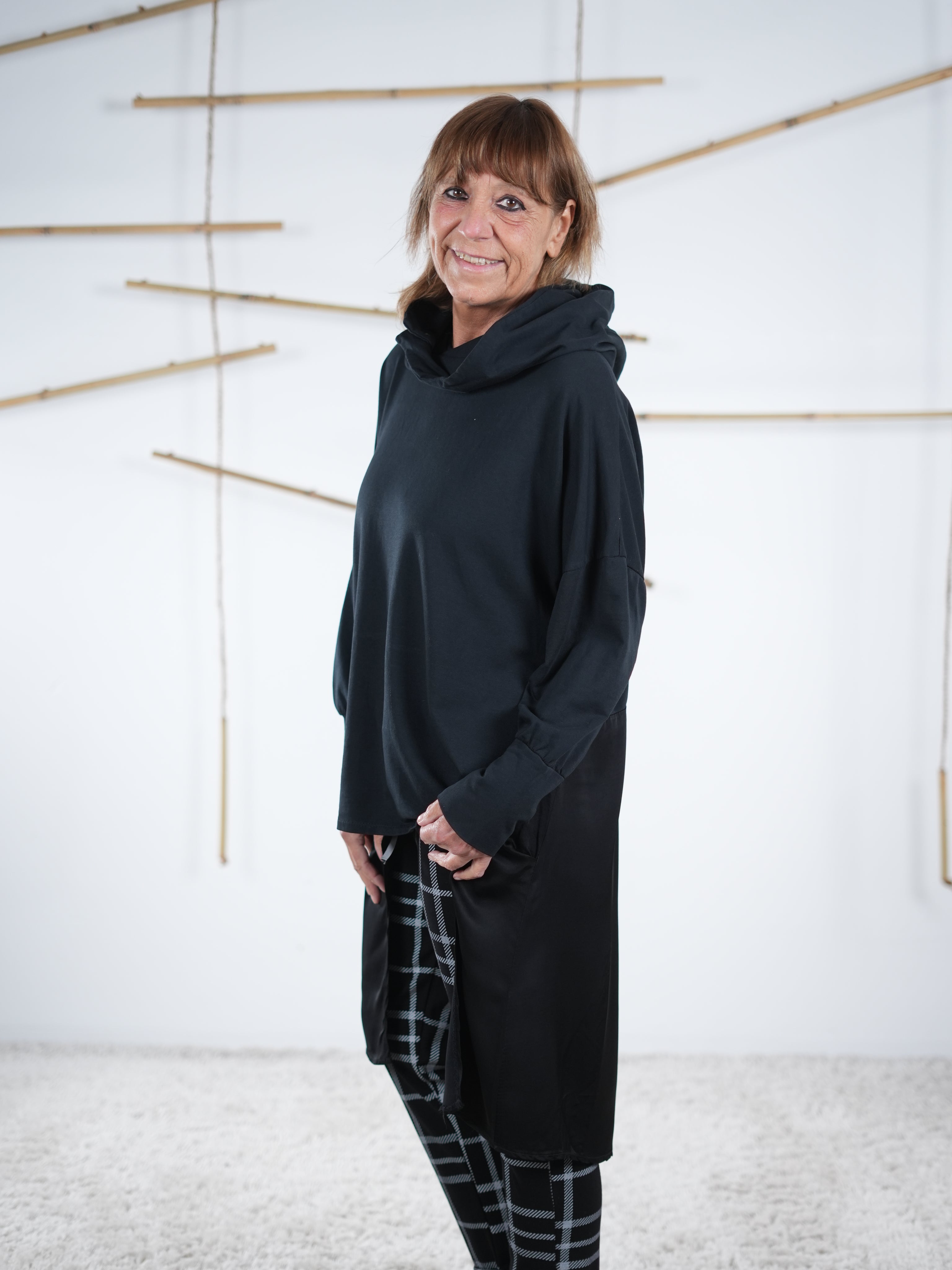 Schwarze Tunika mit Satin-Einsatz, seitlich schräg von hinten fotografiert, lang geschnitten.