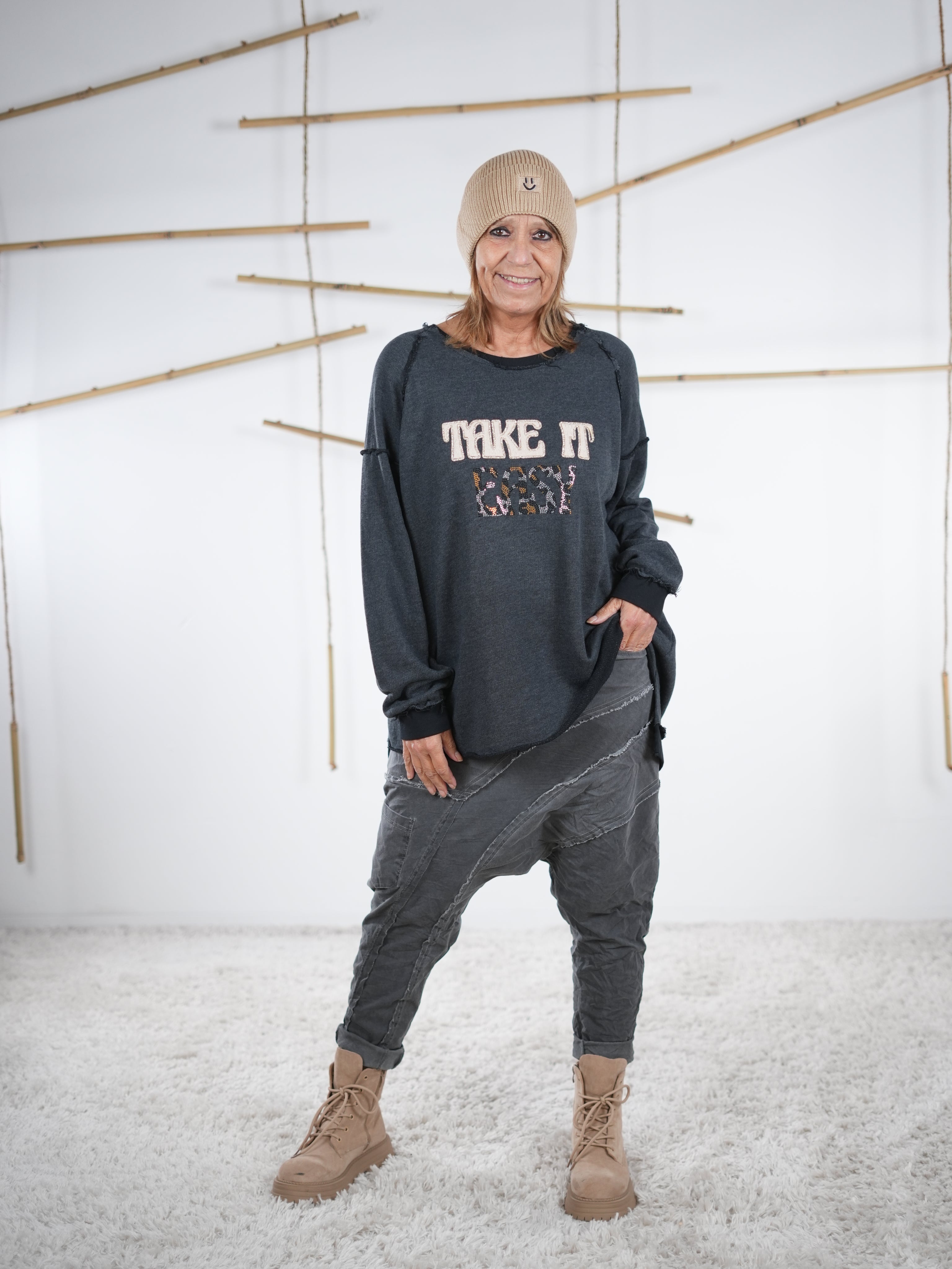 Frau trägt ein anthrazitfarbenes Vokuhila-Sweatshirt mit ‚Take It Easy‘ Schriftzug, lässig getragen