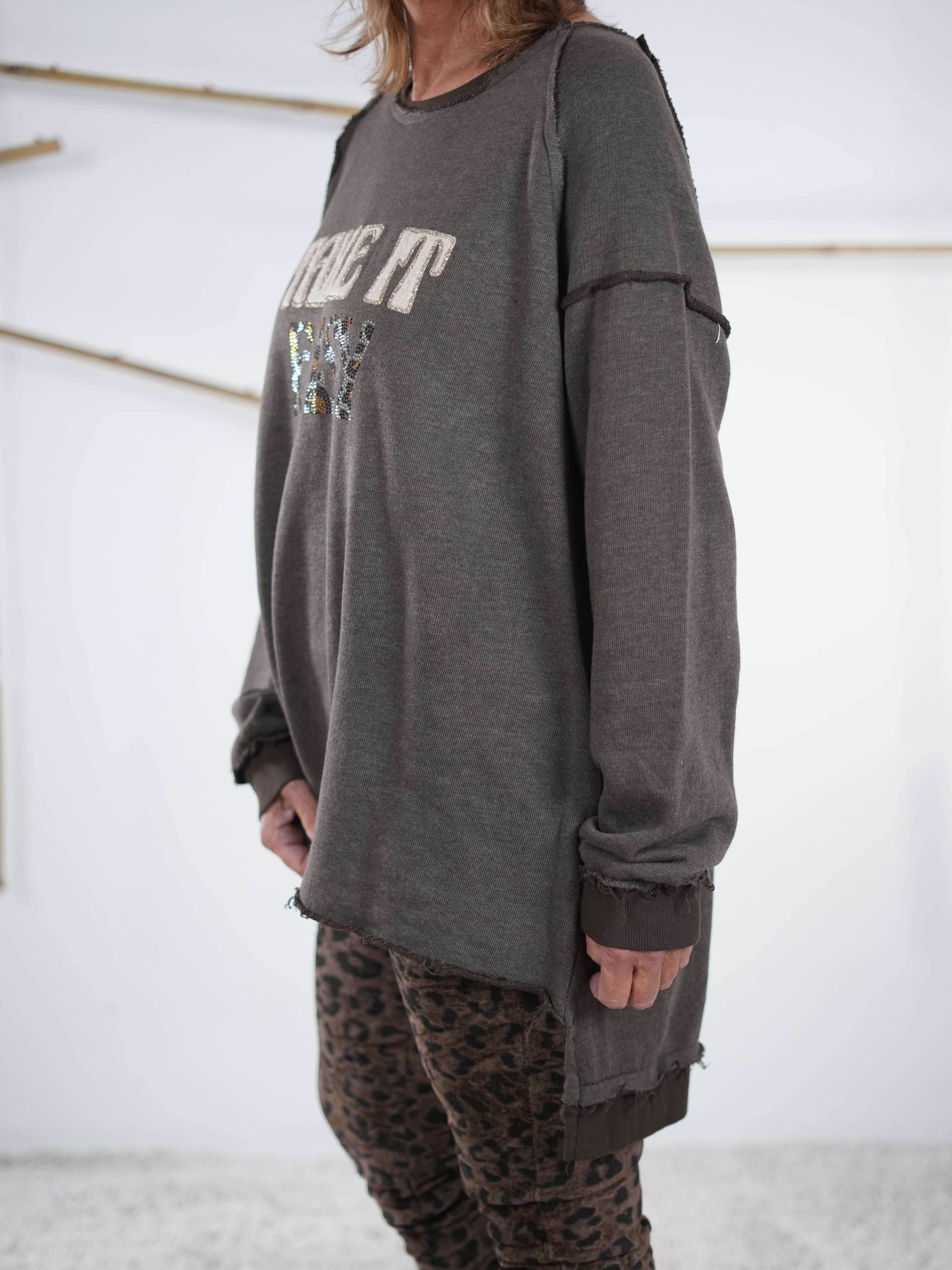 Rückansicht eines schokobraunen Vokuhila-Sweatshirts mit längerem Saum hinten, kombiniert mit Leo-Leggings und neonorangener Mütze.