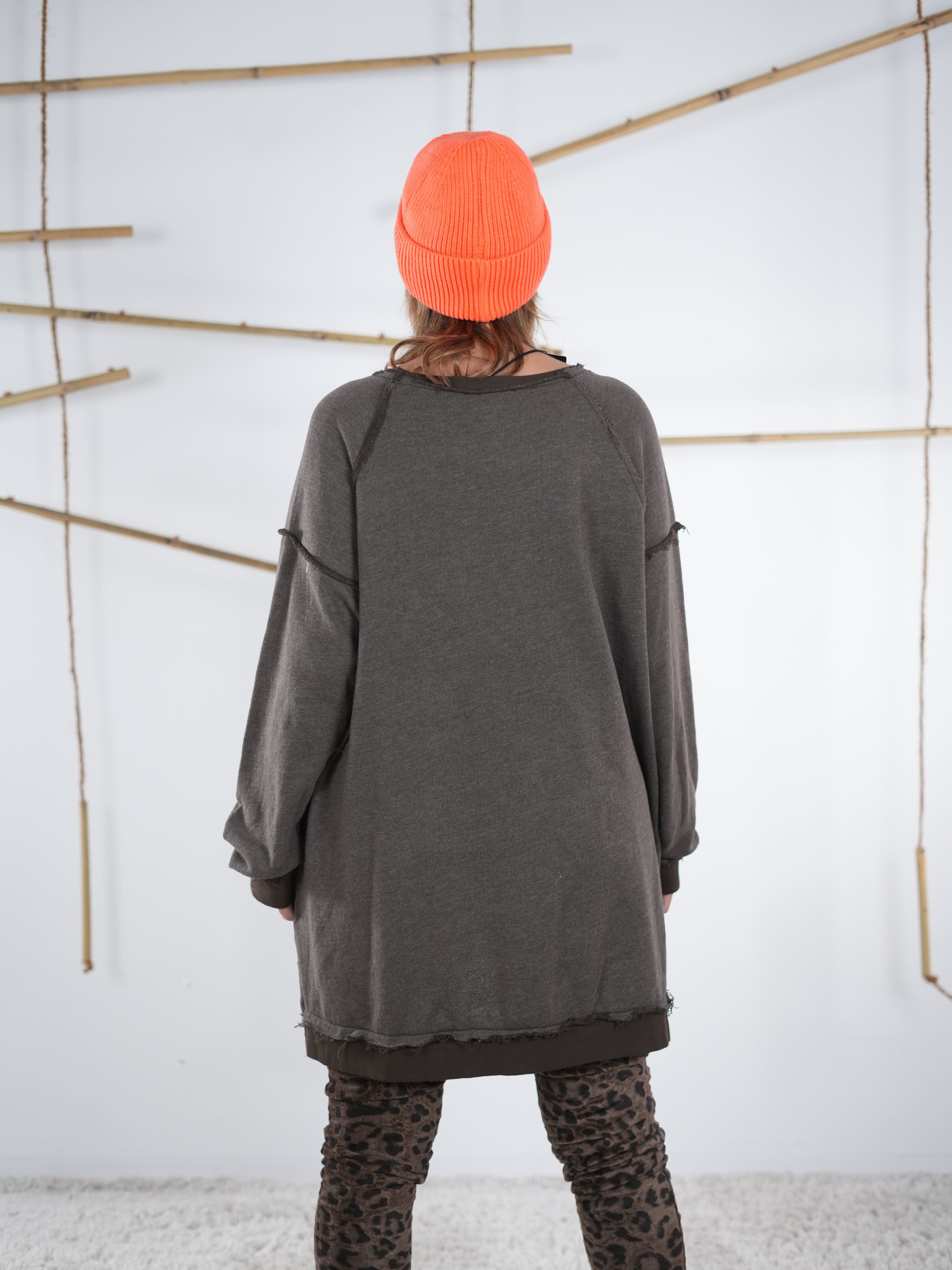 Rückansicht eines schokobraunen Vokuhila-Sweatshirts mit längerem Saum hinten, kombiniert mit Leo-Leggings und neonorangener Mütze.