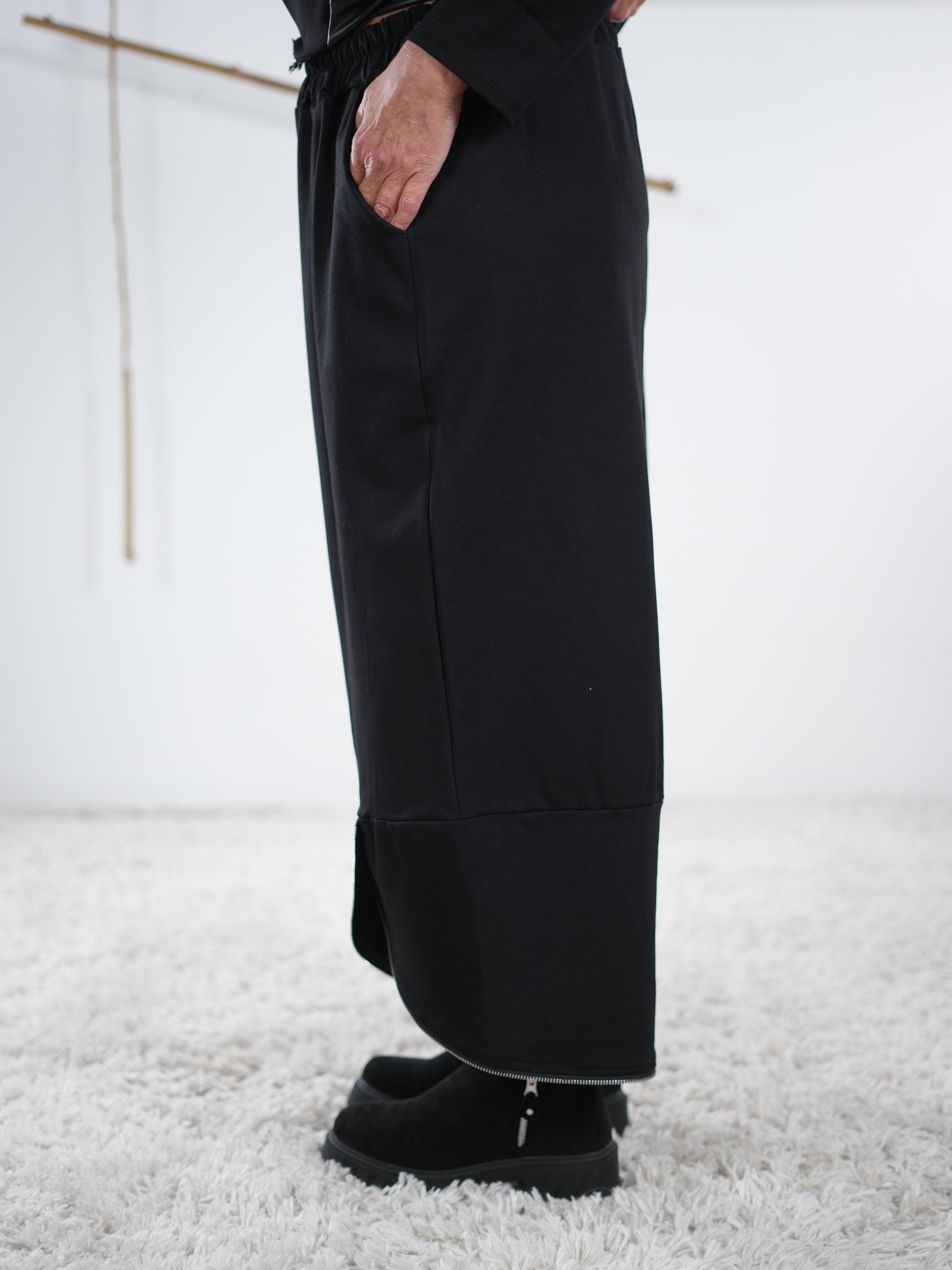 Seitliche Ansicht der schwarzen weiten Hose mit Zipper-Details am Beinabschluss