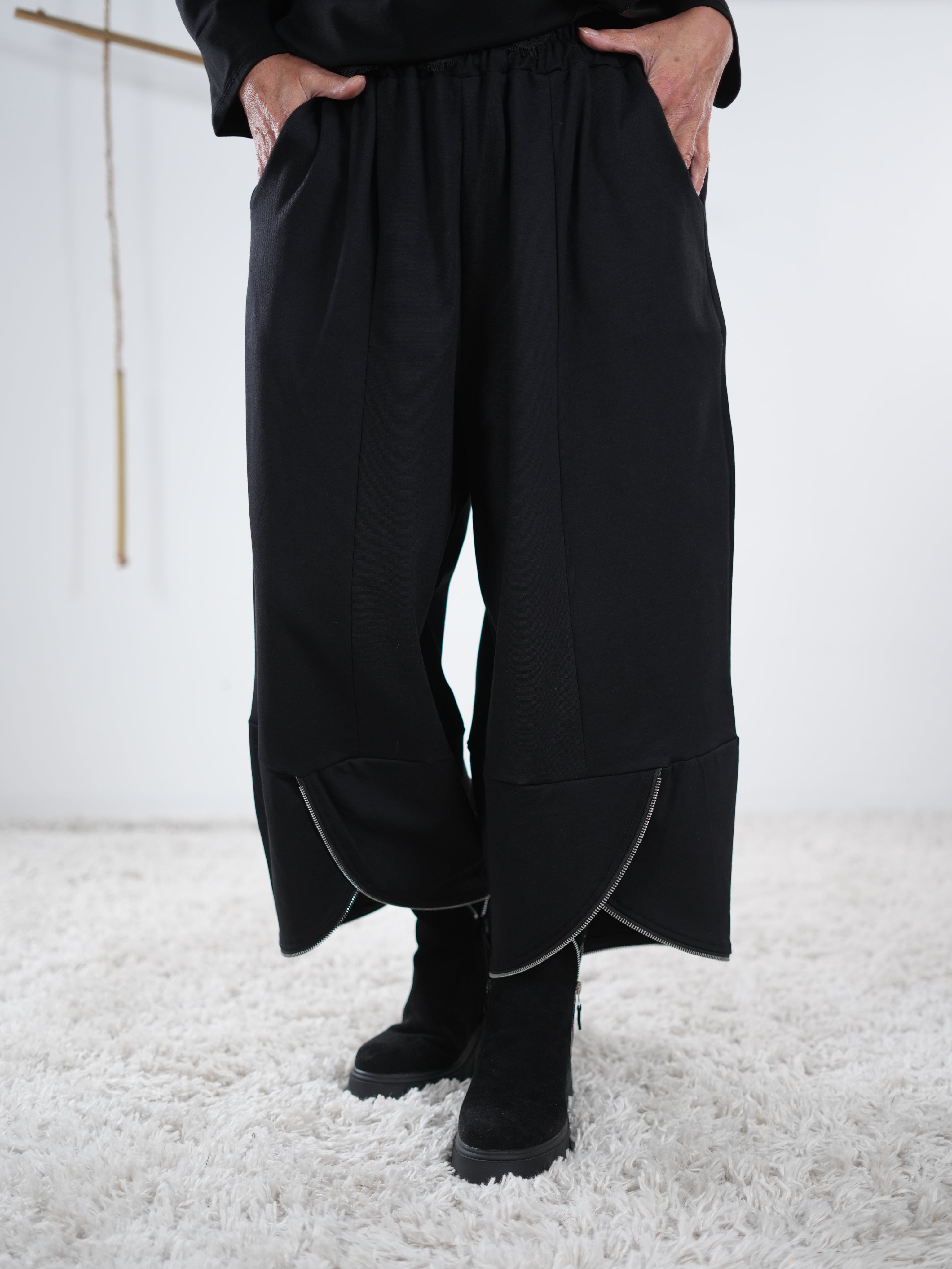 Marion trägt eine Schwarze weite Hose mit elastischem Bund und asymmetrischem Beinabschluss mit Zipper