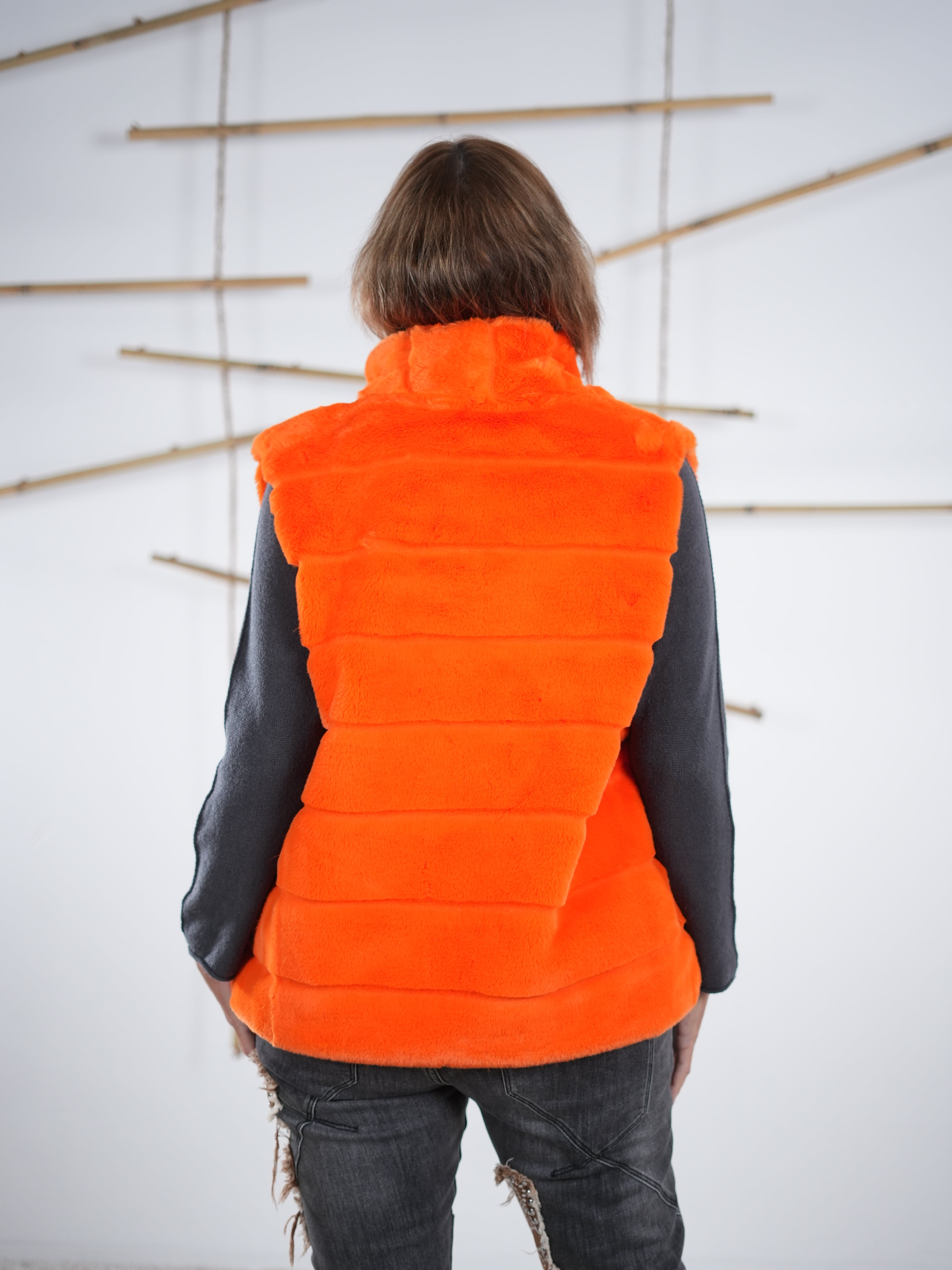 Marion präsentiert das Rückenteil der flauschigen Weste in orange.