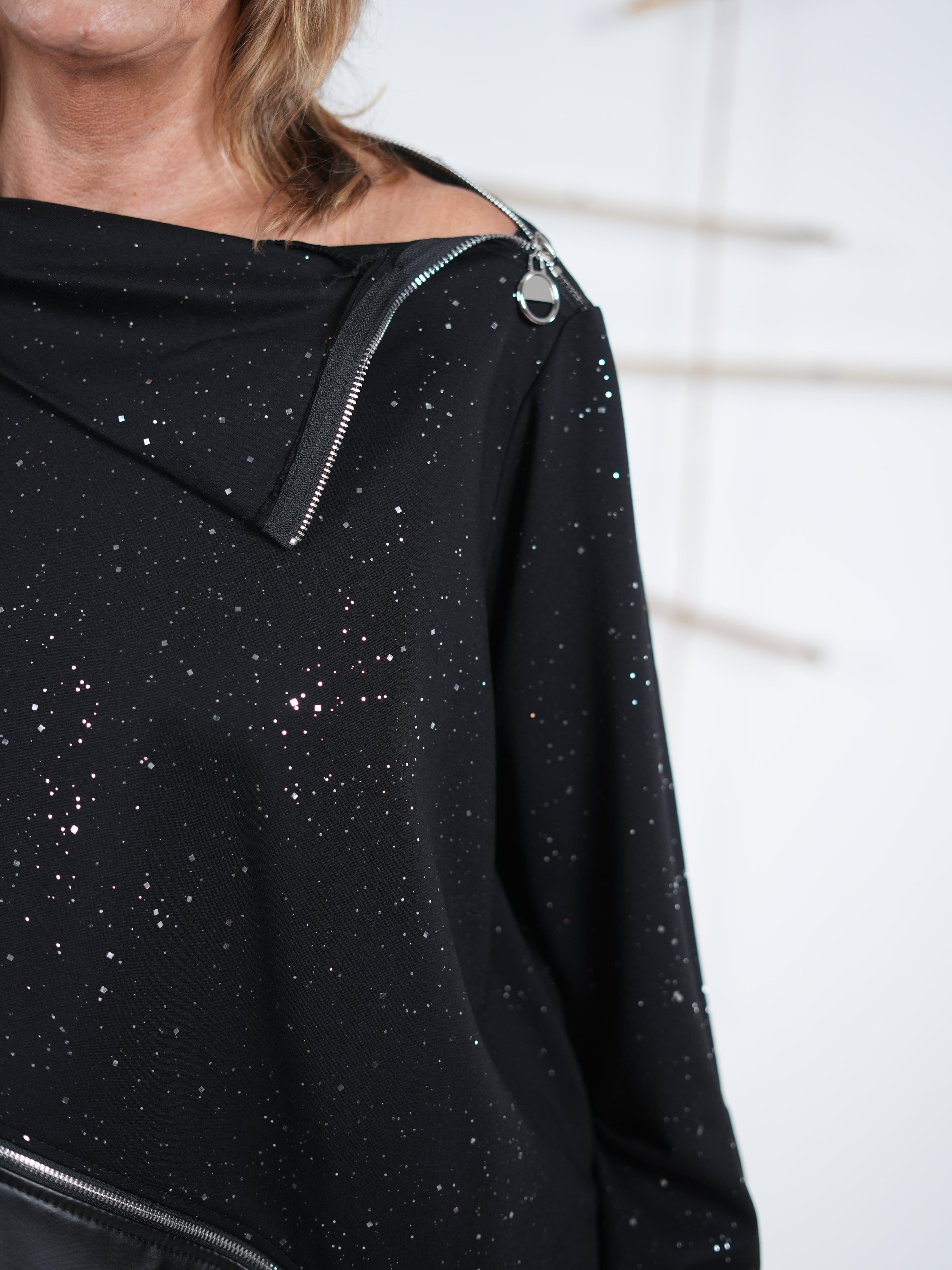 Detailaufnahme des schrägen Reißverschlusses am schwarzen Glitzer-Pulli