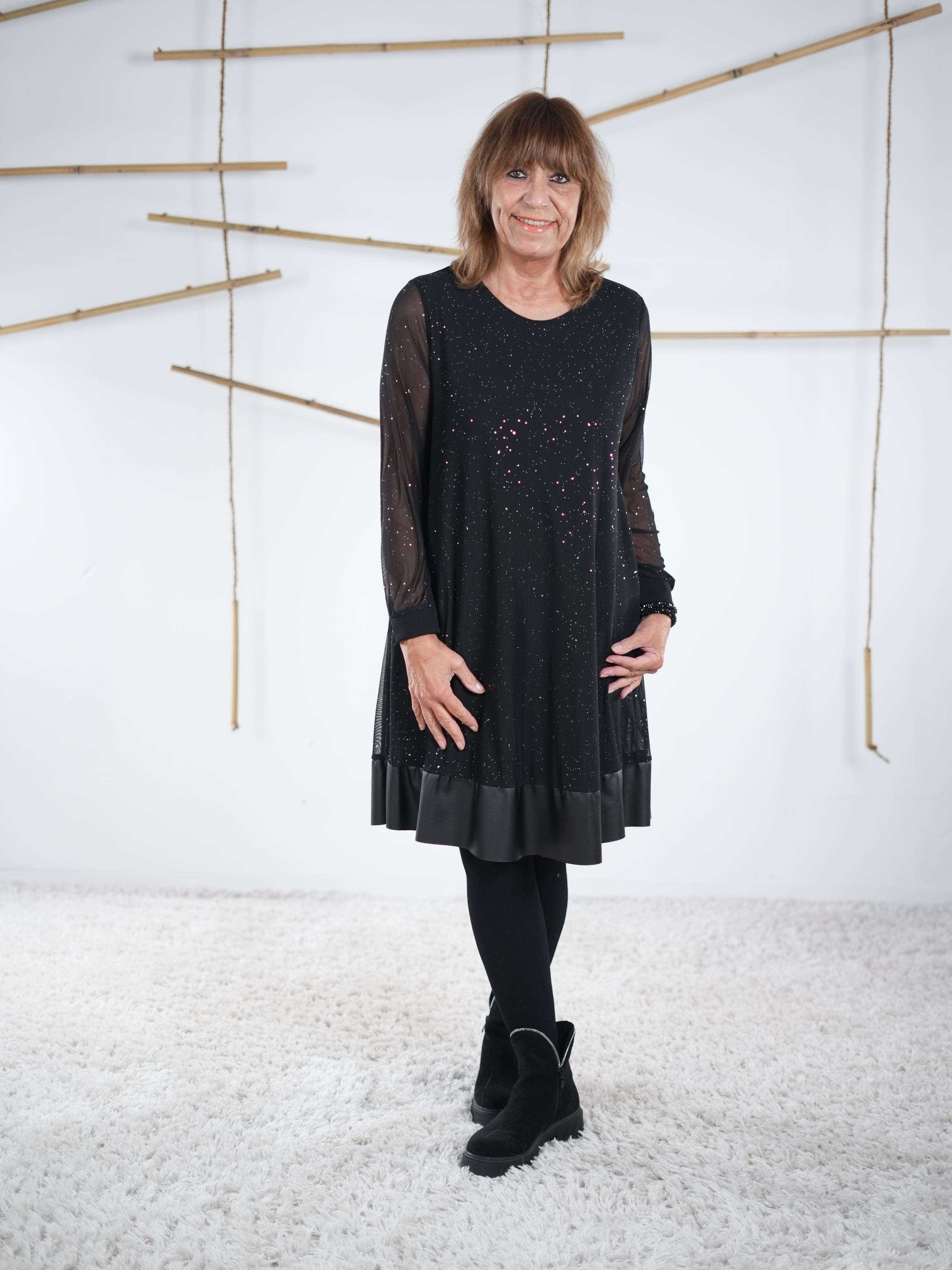 Schwarzes Glitzerkleid mit transparenten Ärmeln und Kunstleder-Saum, vorne getragen