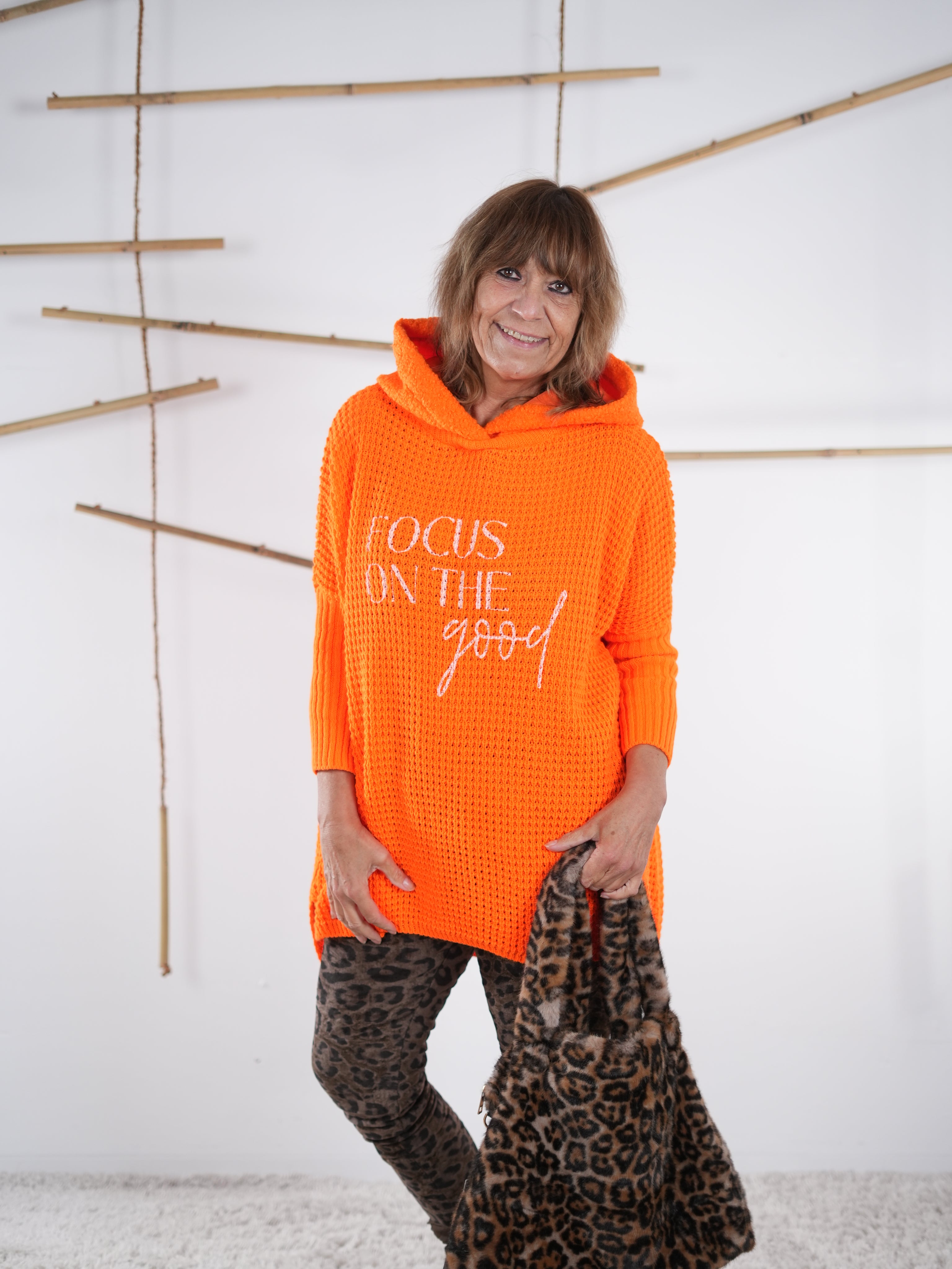 Orangefarbener Grobstrickpulli mit Kapuze und überschnittenen Ärmeln, locker getragen.