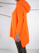 Seitliche Ansicht eines orangefarbenen Grobstrickpullis mit Kapuze und längerem Rückenteil.