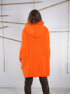 Rückansicht eines orangefarbenen Grobstrickpullis mit Kapuze und Vokuhila-Schnitt.