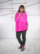 Lässiger Grobstrickpulli in Pink mit Schriftzug, Kapuze und Vokuhila-Schnitt in der Frontansicht.