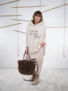 flauschiger Grobstrickpulli mit schwarzem Schriftzug in sand, kombiniert mit einer Baggy und süßen Accessoires.