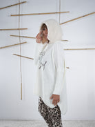 flauschiger Grobstrickpulli mit schwarzem Schriftzug in wollweiß. Marion präsentiert die seitliche Ansicht des Pullis.