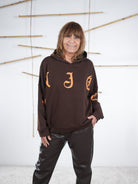 Damen-Hoodie in Schokobraun mit großem orangefarbenem Letter-Print vorne, kombiniert mit einer dunkelbraunen Kunstlederhose, mit Kapuze