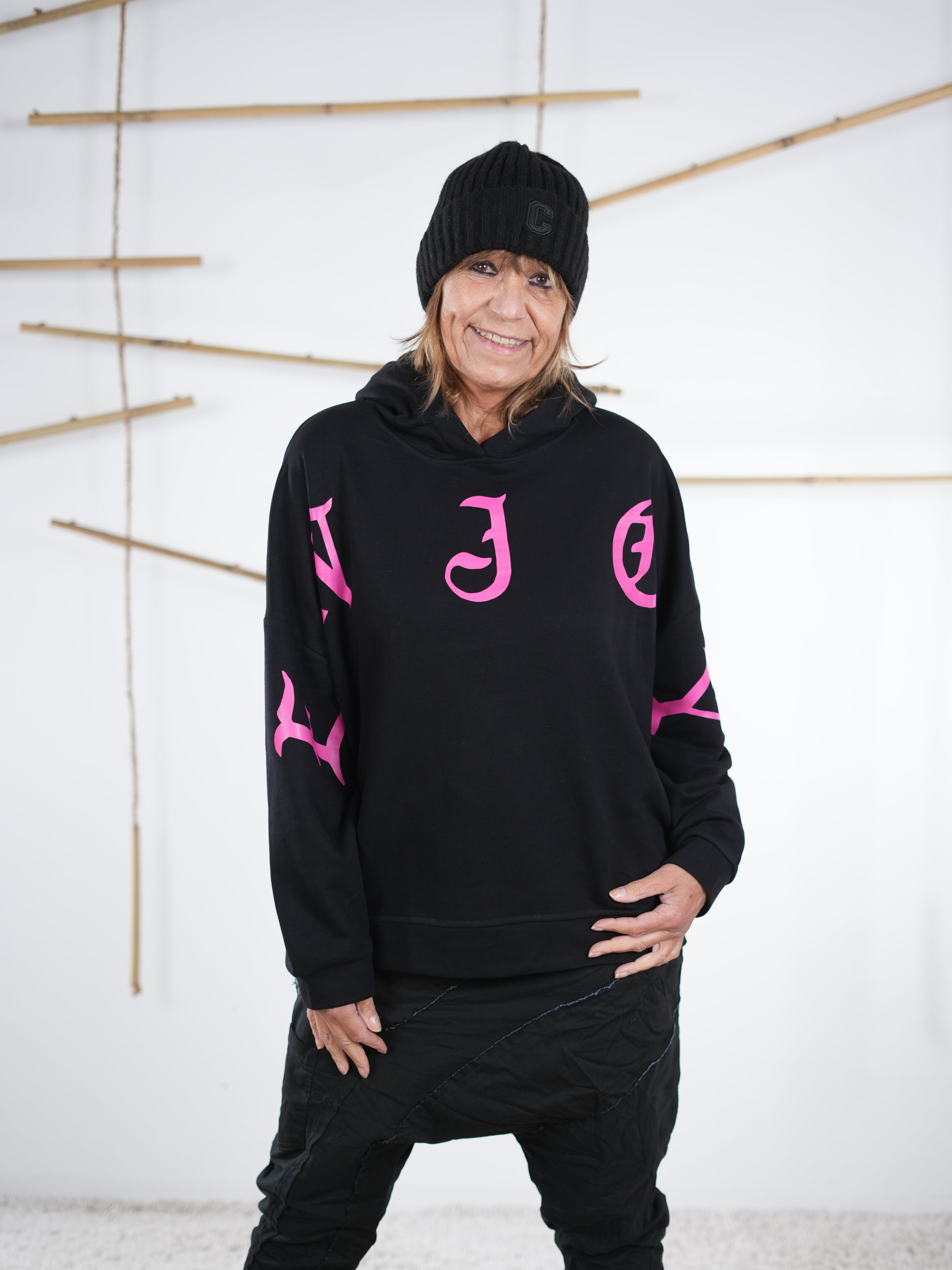 Schwarzer Damen-Hoodie mit pinkem Letter-Print auf Brust und Ärmeln, lässig kombiniert mit schwarzer Hose.