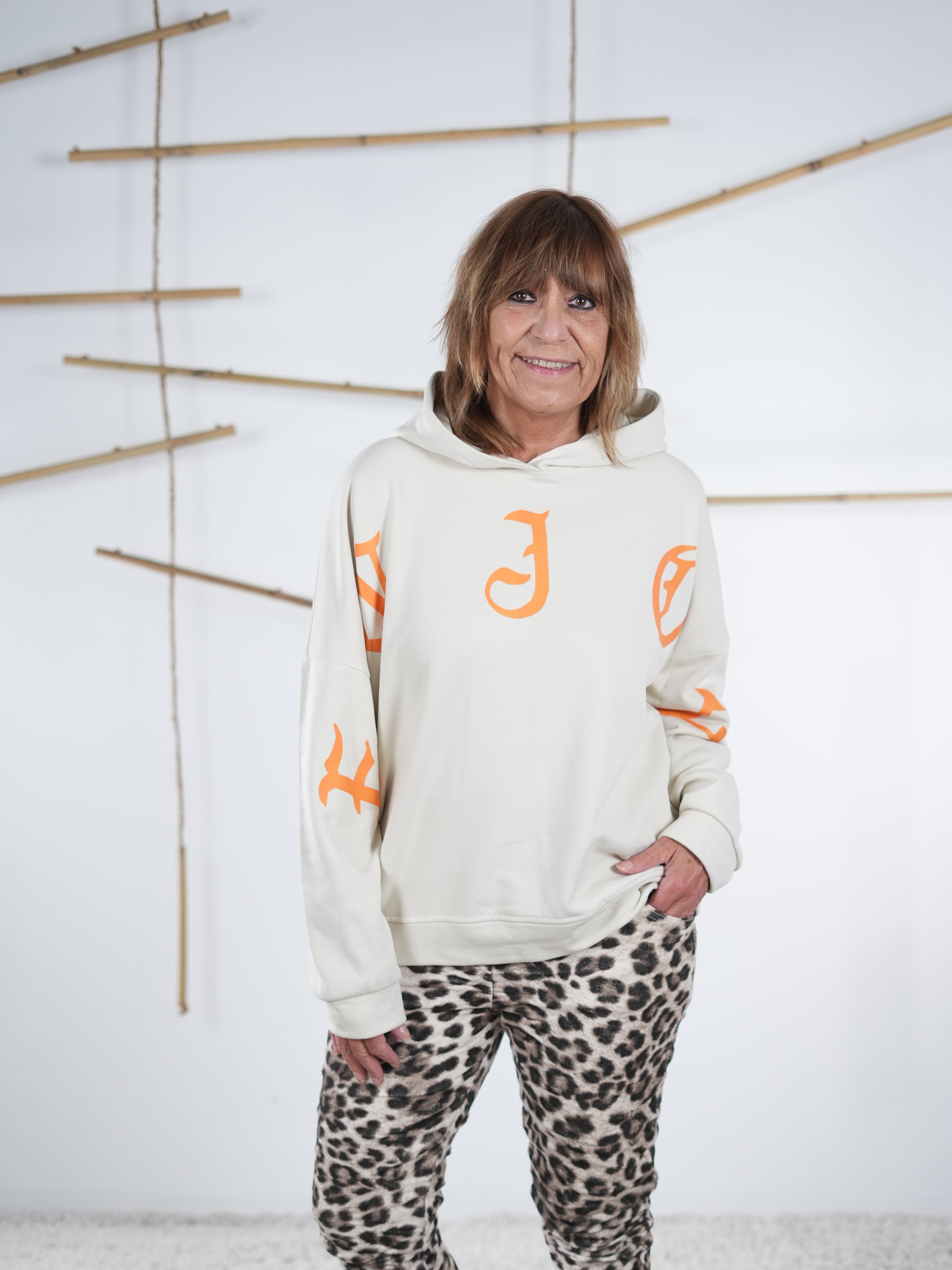 Wollweißer Damen-Hoodie mit orangefarbenem Letter-Print, gestylt zu einer schmalen Leopardhose.