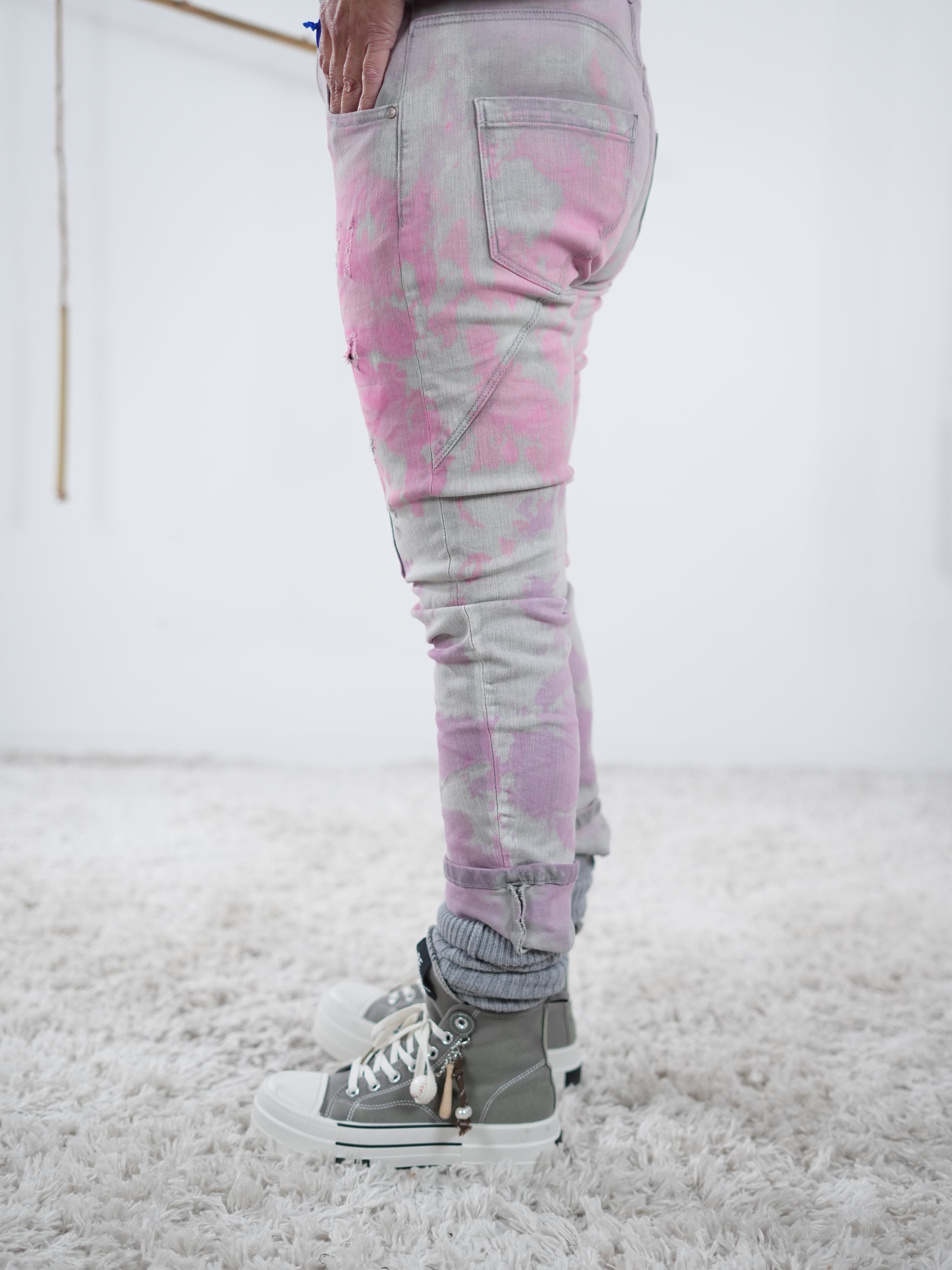 Seitliche Ansicht auf deine eng anliegende, graue Jeans mit pinken Details. Die Jeans hat einen breiten Abschluss.