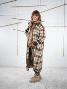 Seitenansicht eines langen karierten Fleece-Mantels in Beige-Braun, getragen von einer Frau im Studio.