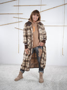 Frau trägt einen langen karierten Fleece-Mantel in Beige-Braun, kombiniert mit Hoodie und Jeans, frontal fotografiert