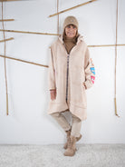 Langer beige Mantel mit Zipper und bunten Comic-Patches am Arm