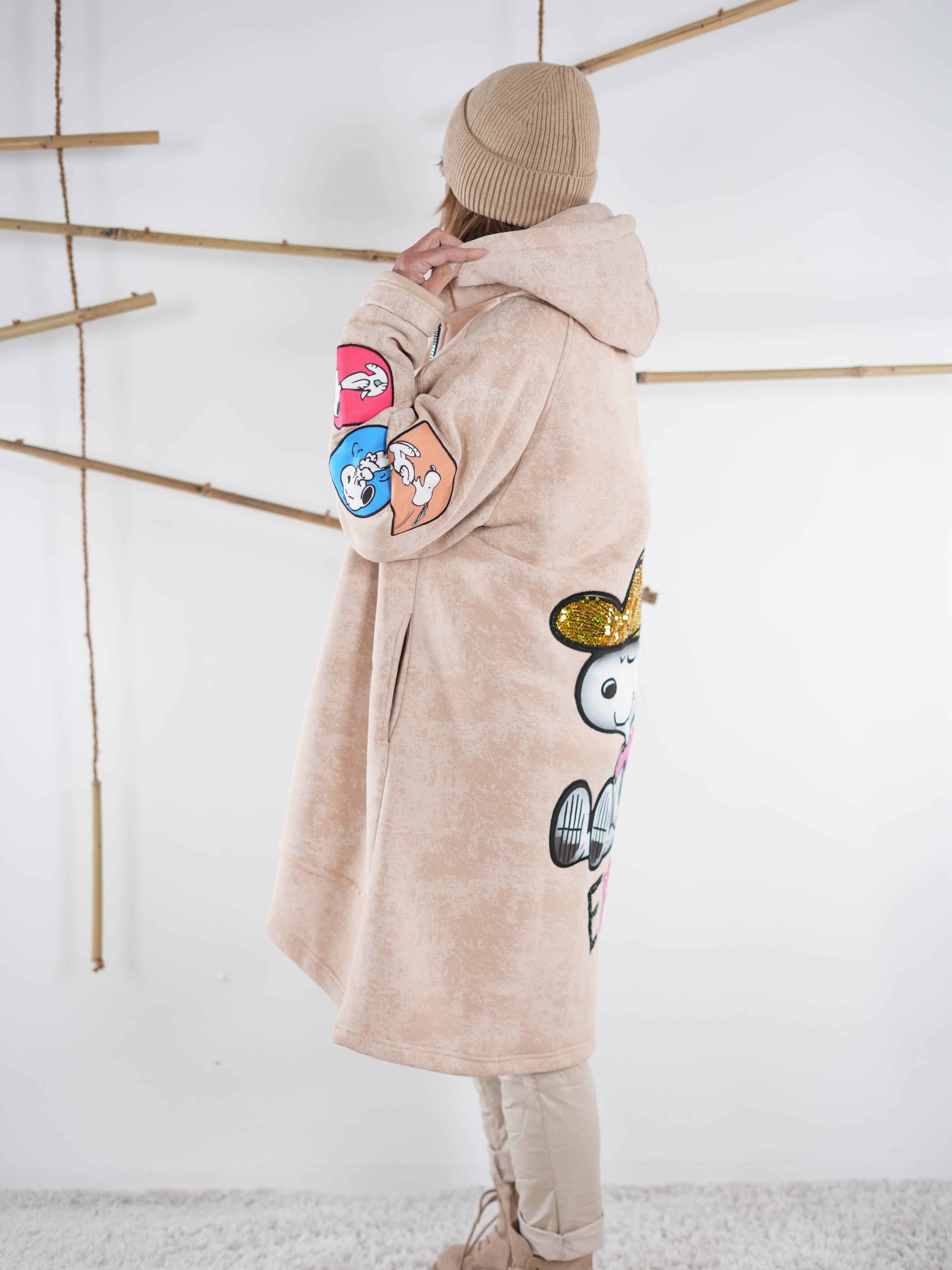 Beiger Mantel seitlich mit bunten Comic-Patches am Ärmel