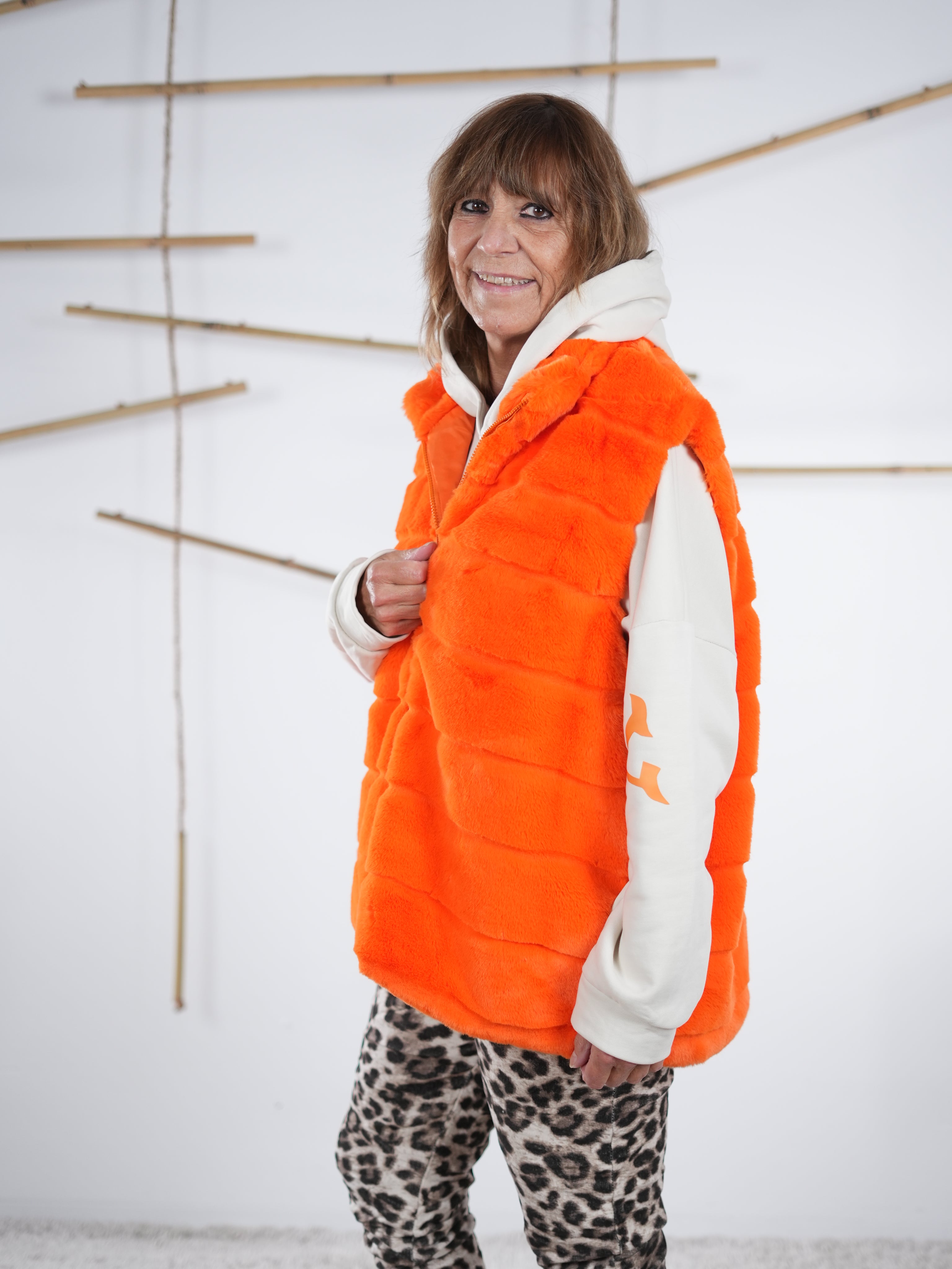 Seitliche Ansicht einer orangefarbenen Flausch-Weste mit Reißverschluss und kuscheliger Oberfläche.