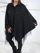 Nahaufnahme der schwarzen Tunika. Der Fokus liegt auf dem asymmetrischen, weiten Schnitt. 