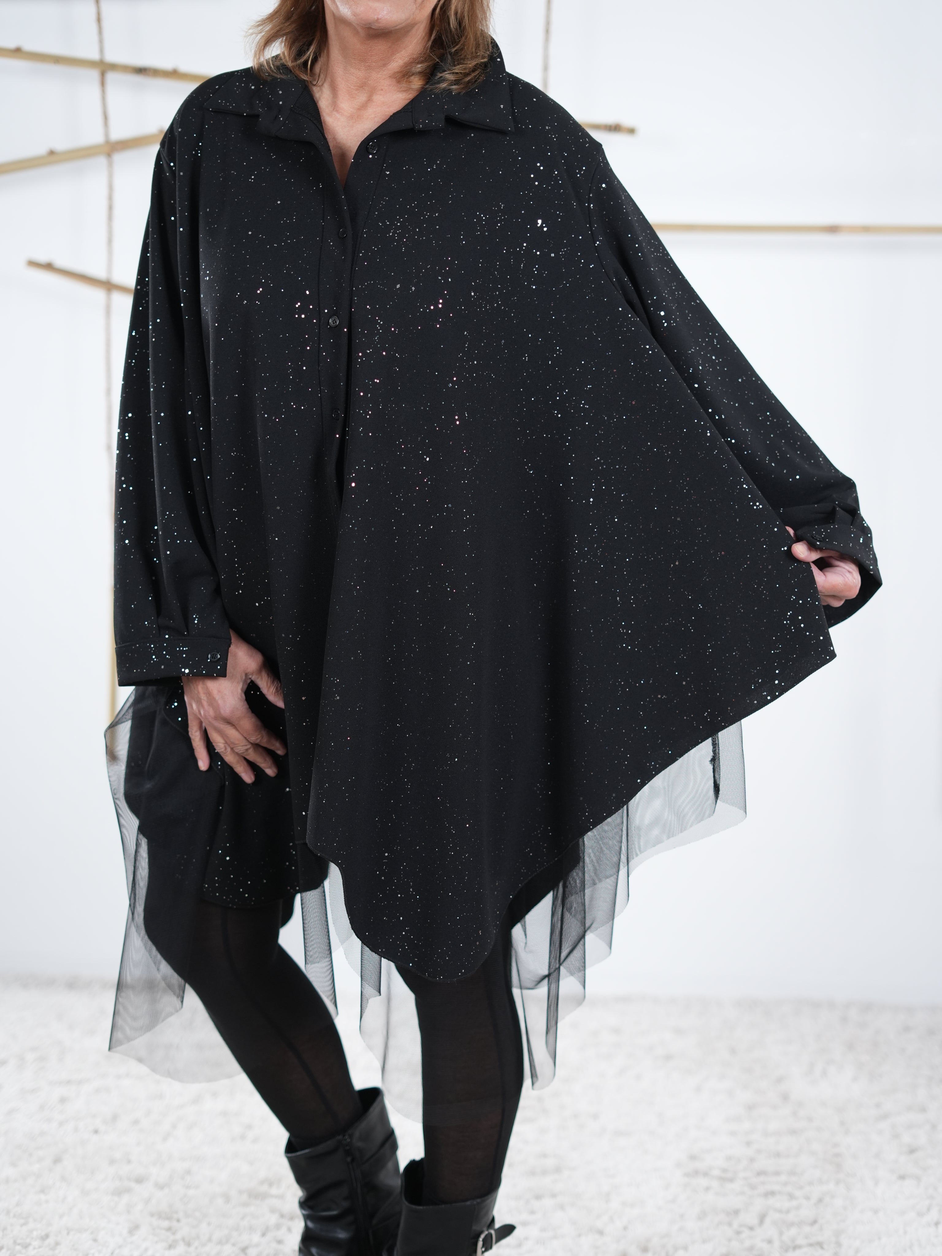 Nahaufnahme der schwarzen Tunika. Der Fokus liegt auf dem asymmetrischen, weiten Schnitt. 