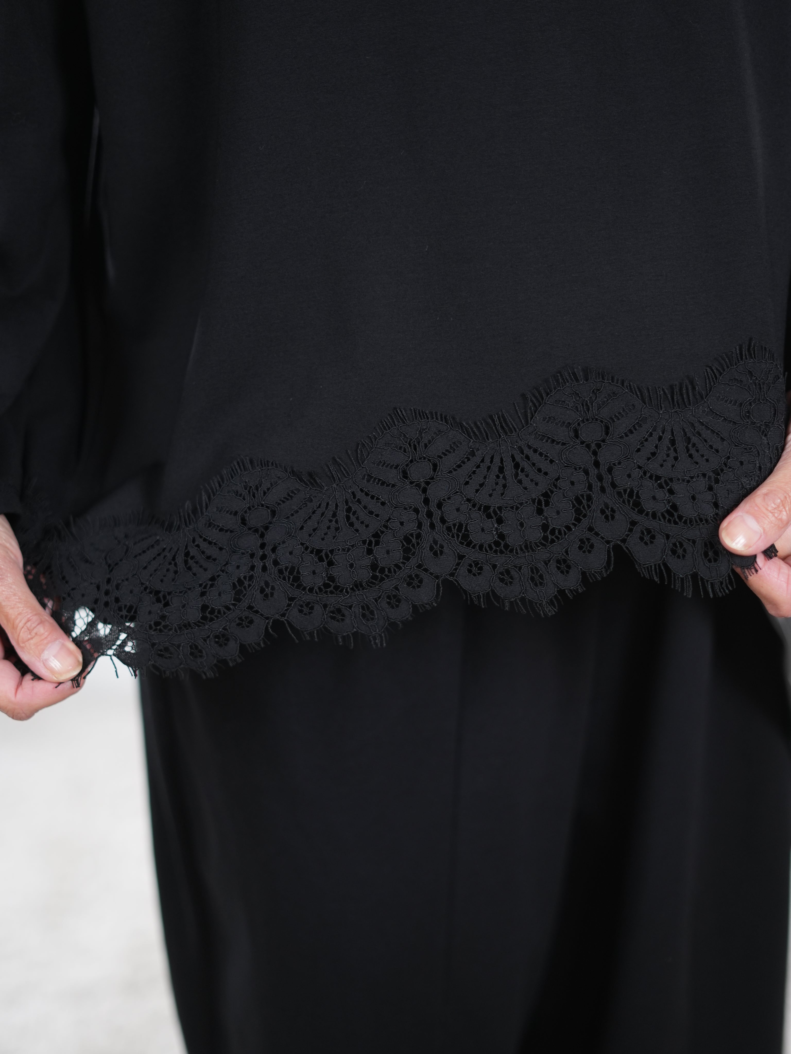 Detaillierte Ansicht eines lockeren, schwarzen Pullis mit Spitze verziert.