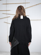 Rückansicht eines schwarzen Pullis mit Kunstleder-Einsatz und Spitzenkante, locker fallender Schnitt