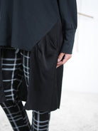 Detailaufnahme der schwarzen Damen-Tunika mit Satin-Einsatz an der Seite, kombiniert mit karierten Hosen.