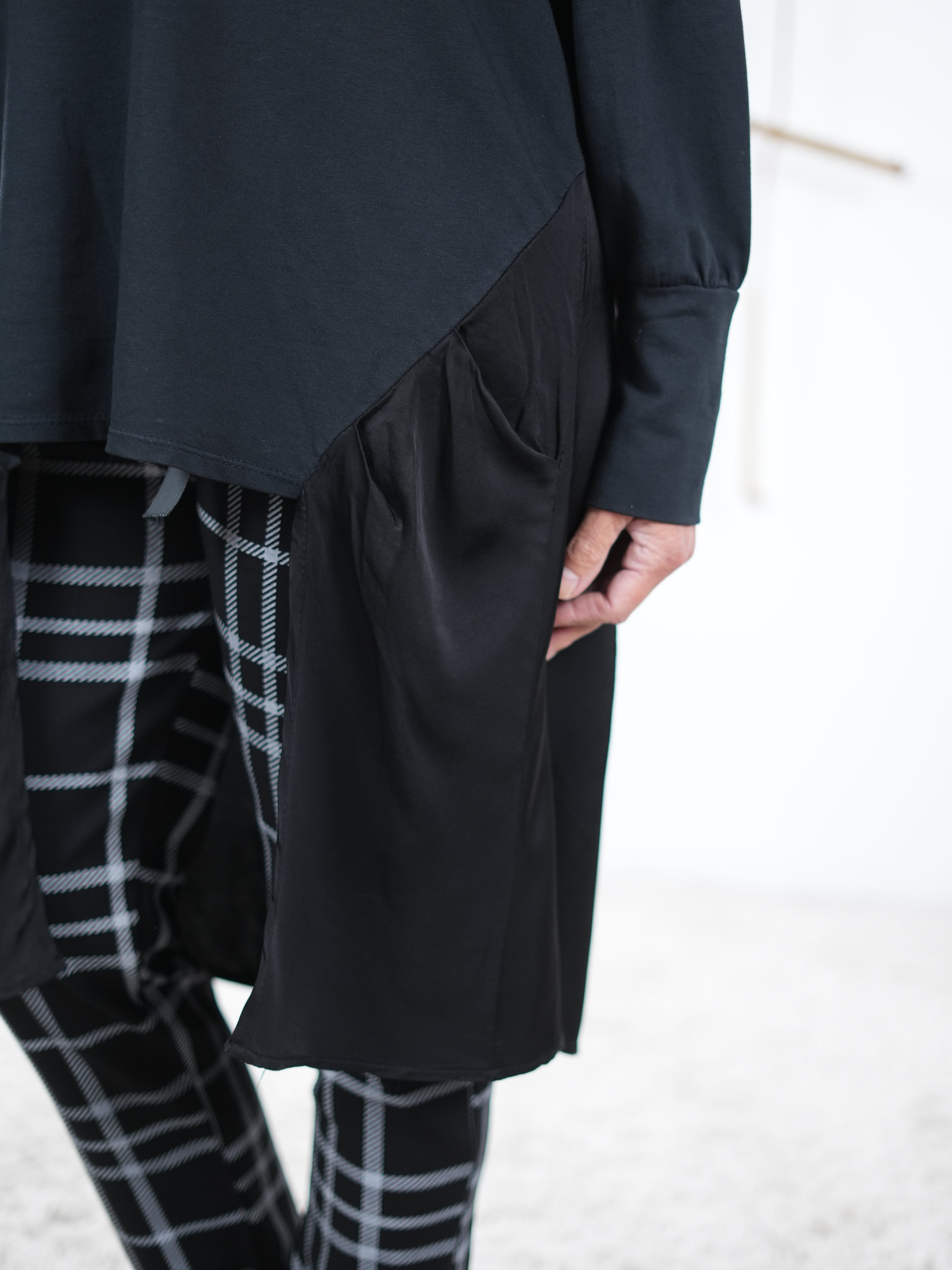 Detailaufnahme der schwarzen Damen-Tunika mit Satin-Einsatz an der Seite, kombiniert mit karierten Hosen.
