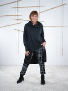 Schwarze Damen-Tunika mit seitlichem Satin-Einsatz in der frontalen Ansicht, locker geschnitten, kombiniert mit Karohose.