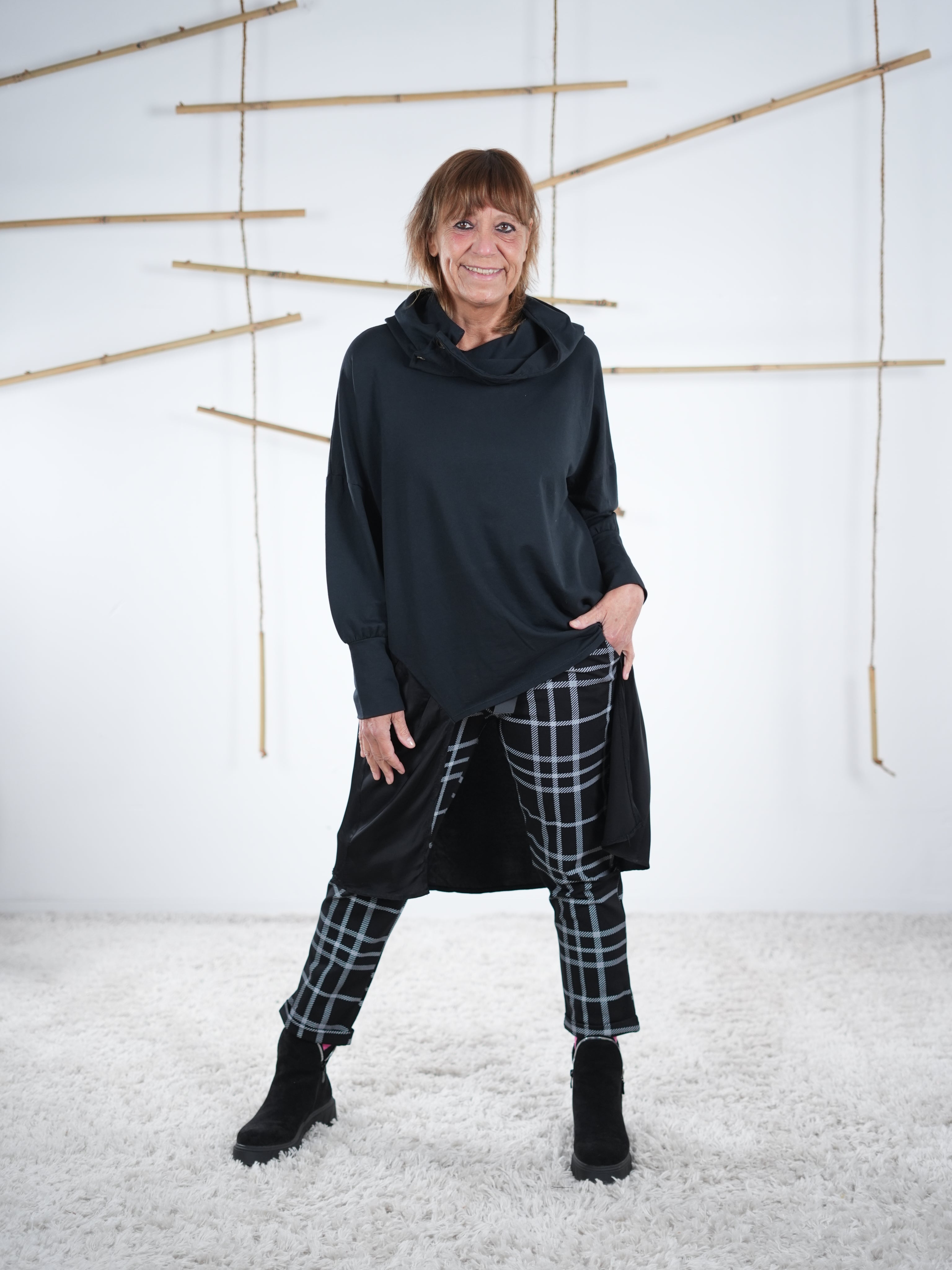 Schwarze Damen-Tunika mit seitlichem Satin-Einsatz in der frontalen Ansicht, locker geschnitten, kombiniert mit Karohose.