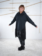 Schwarze Oversize-Tunika mit Satin-Einsatz und Kapuze, Tragefoto mit ausgestreckten Armen.