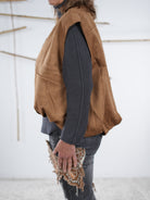 Seitliche Ansicht einer camel­farbenen Velours-Weste in Lederoptik mit Gummizug am Abschluss.