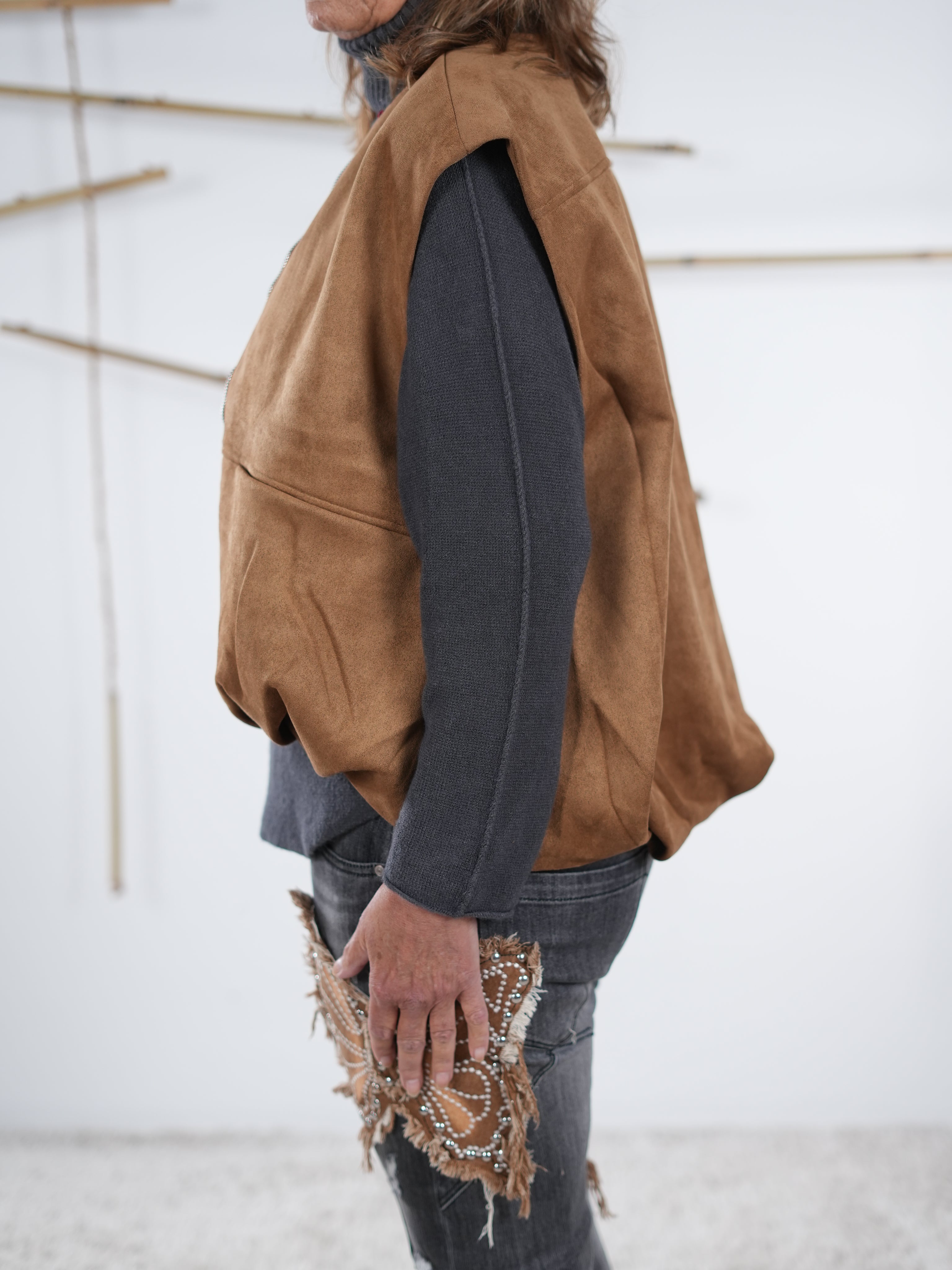 Seitliche Ansicht einer camel­farbenen Velours-Weste in Lederoptik mit Gummizug am Abschluss.