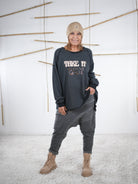 Frau trägt ein anthrazitfarbenes Vokuhila-Sweatshirt mit ‚Take It Easy‘ Schriftzug, lässig getragen