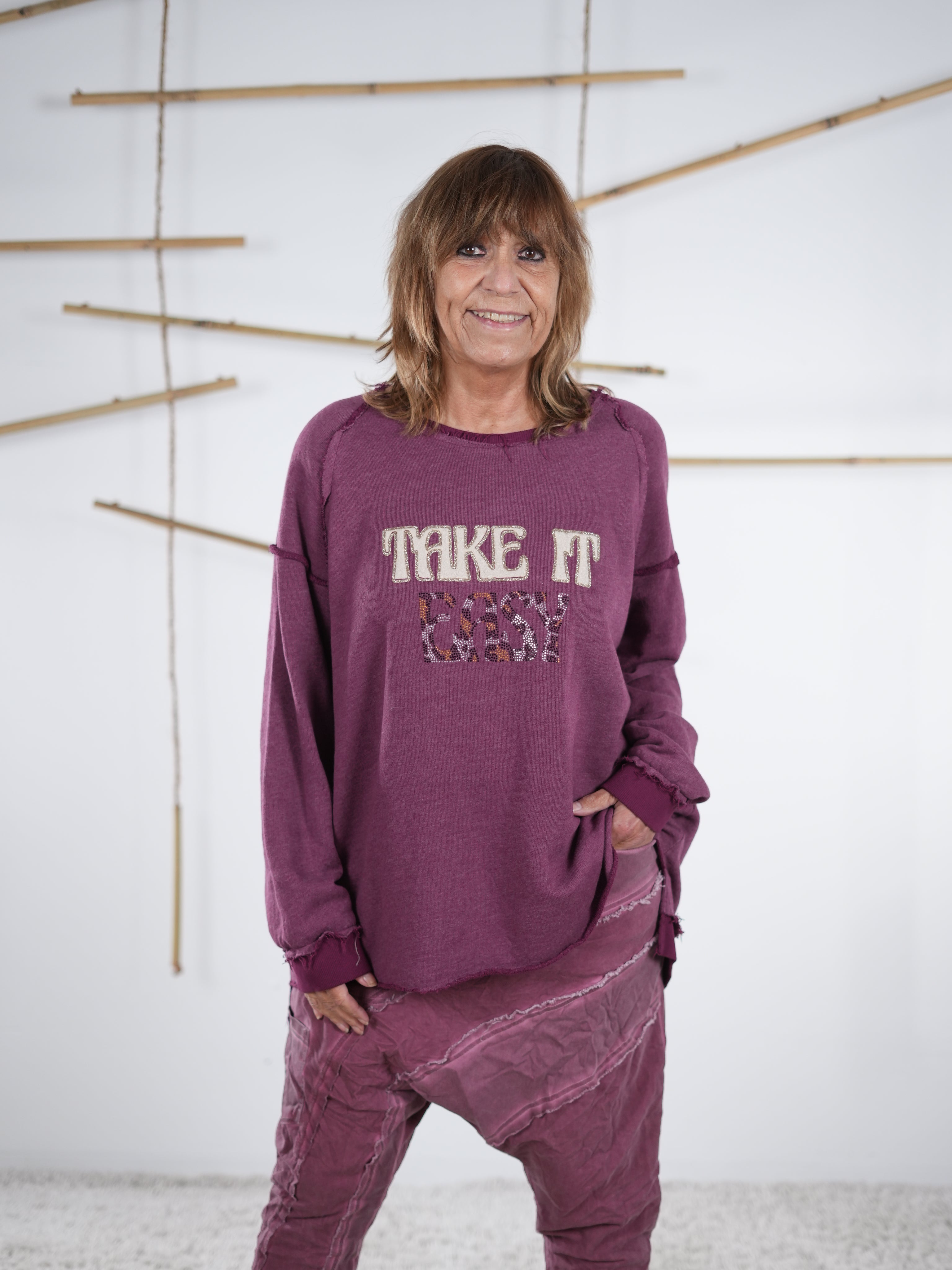 Frau trägt ein beerenfarbenes Vokuhila-Sweatshirt mit ‚Take It Easy‘ Schriftzug und passender Hose in Beere.