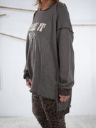 Rückansicht eines schokobraunen Vokuhila-Sweatshirts mit längerem Saum hinten, kombiniert mit Leo-Leggings und neonorangener Mütze.