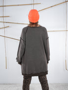 Rückansicht eines schokobraunen Vokuhila-Sweatshirts mit längerem Saum hinten, kombiniert mit Leo-Leggings und neonorangener Mütze.