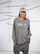 Frau in taupefarbenem Vokuhila-Sweatshirt mit ‚Take It Easy‘ Schriftzug und beigen Boots